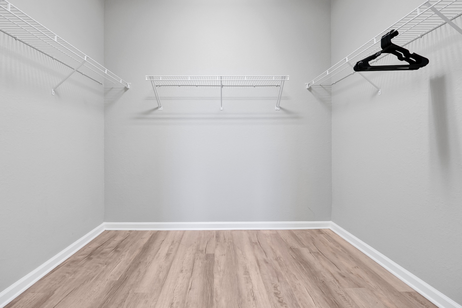 This spacious walk-in closet offers ample hanging and storage space with clean, modern wire shelving along three walls. The light wood-look flooring adds warmth, giving you a bright and organized space to arrange your wardrobe exactly as you like.