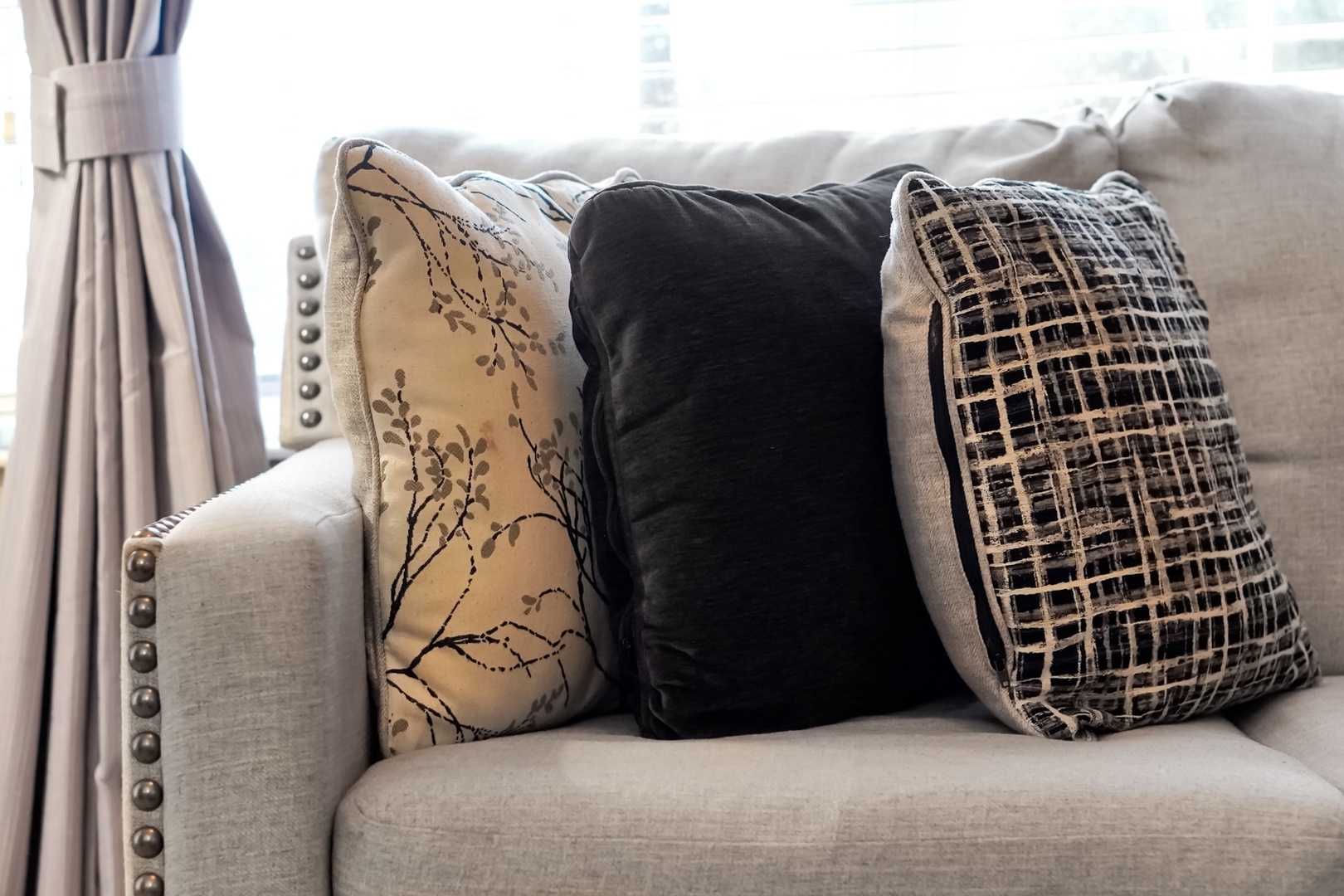 Sink into the plush sofa with layered accent pillows, where natural light streams through the windows and invites you to unwind in effortless comfort.