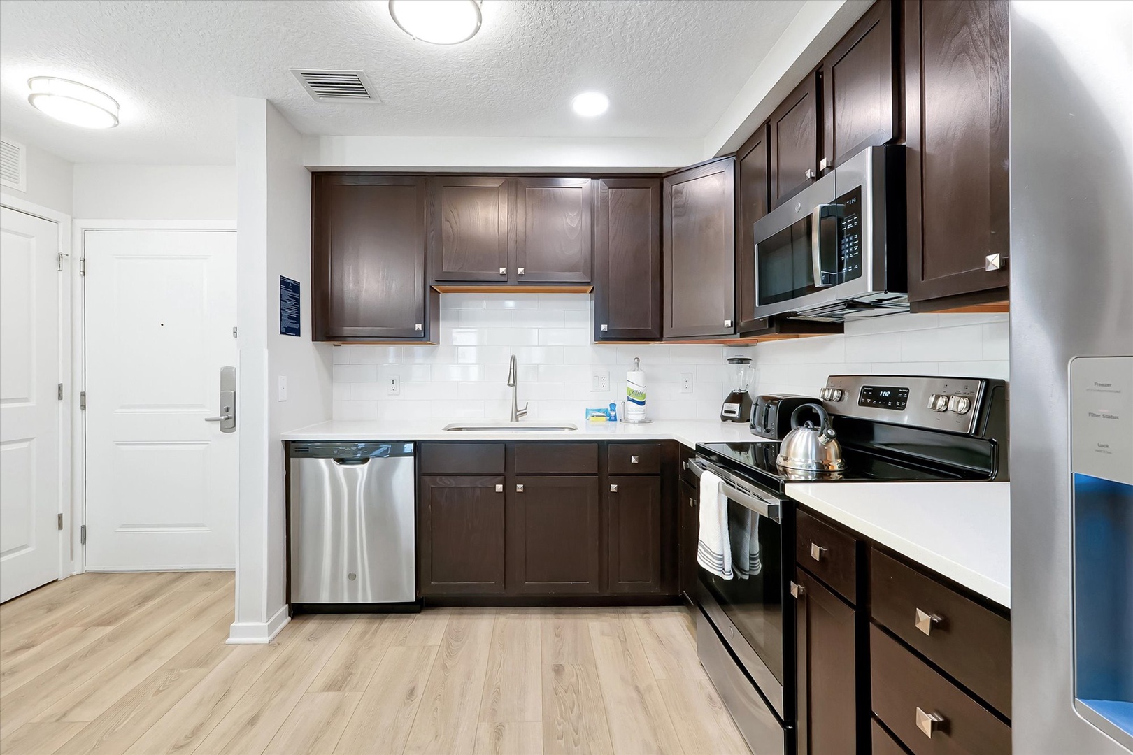 Step into your fully equipped kitchen with stainless steel appliances, rich wood cabinetry, and bright white countertops perfect for preparing meals.