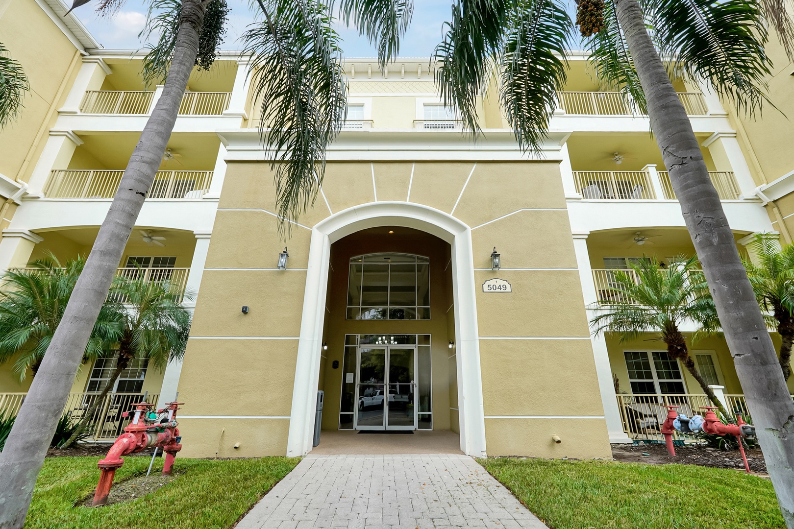 The property entrance is marked by tall palm trees and a distinctive archway, with colorful outdoor seating dotting the landscaped grounds at building 5049.