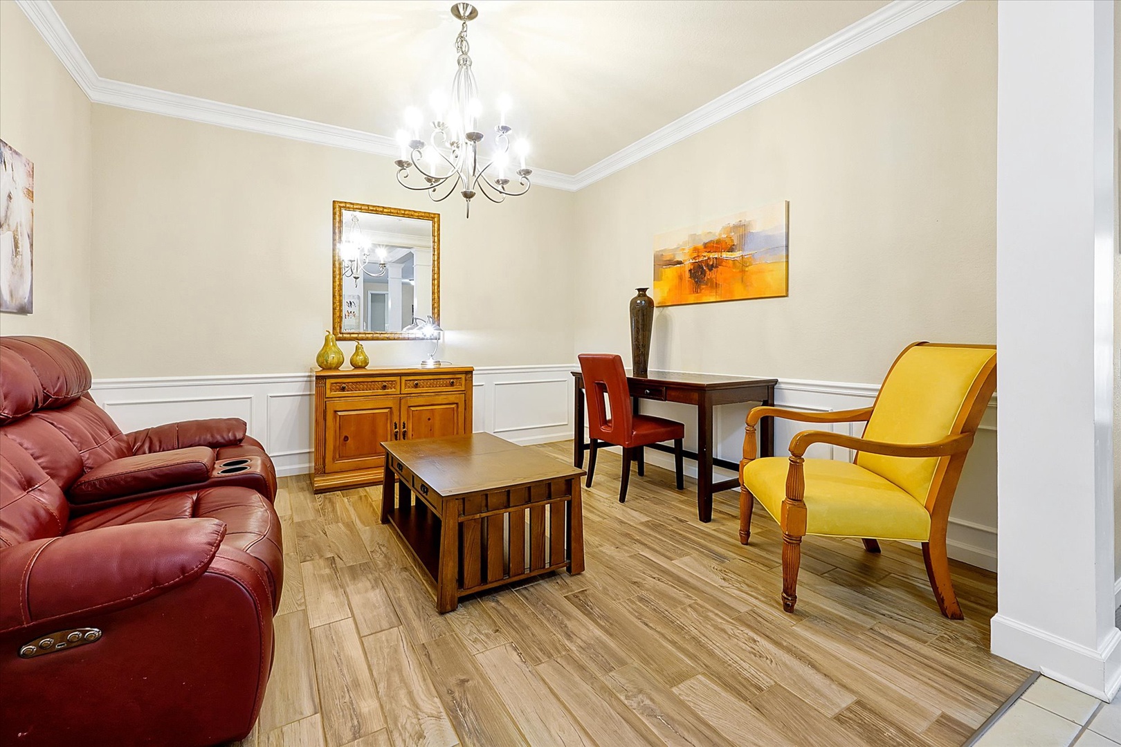 Relax in your elegant living space featuring plush leather seating, warm hardwood floors, and thoughtful touches like artwork and ambient chandelier lighting.