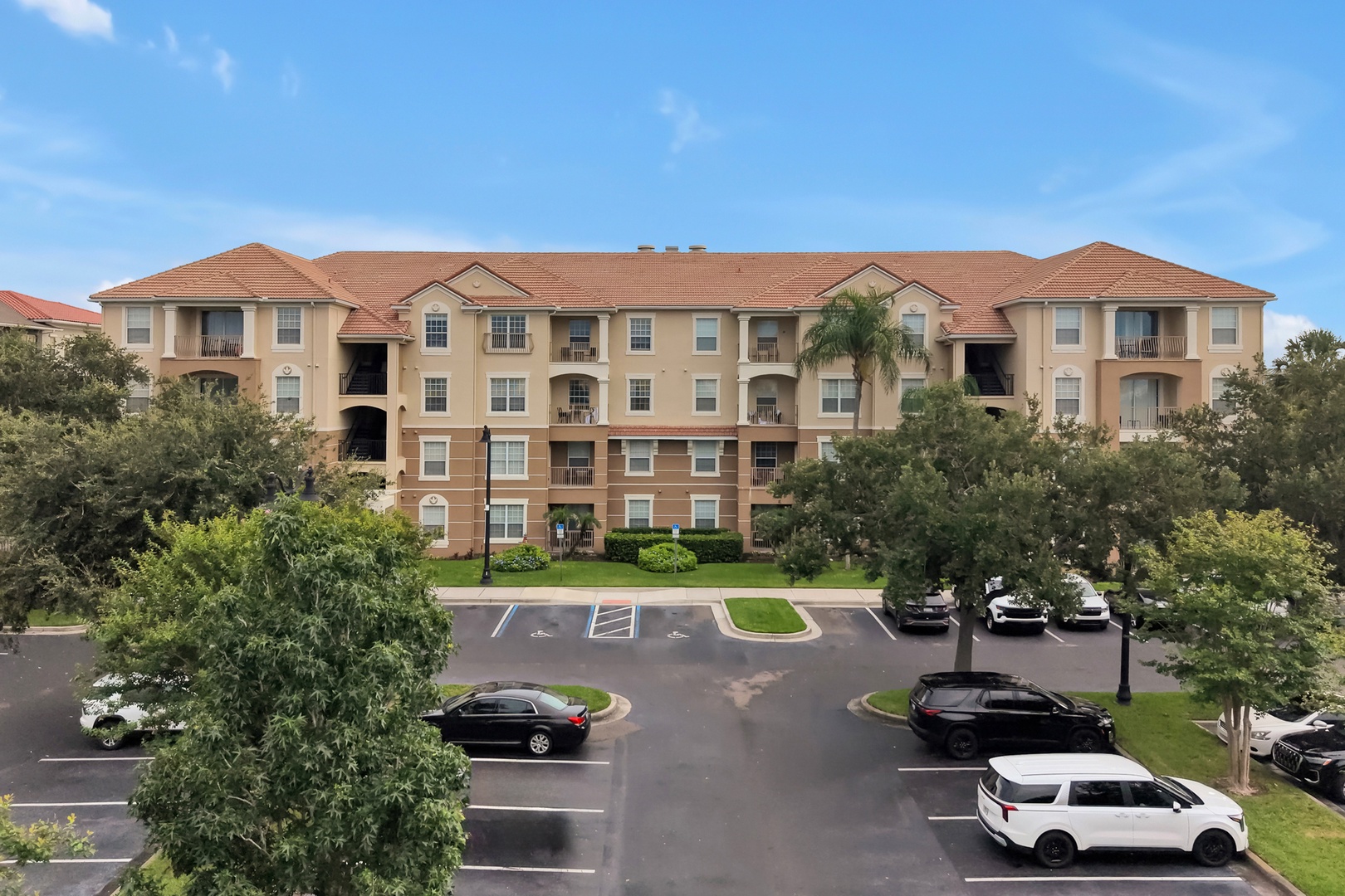 Located in building 5000, right next to the clubhouse. A four-story vacation rental building set in a landscaped area with accessible parking and palm trees, offering a convenient arrival experience in a sunny location.