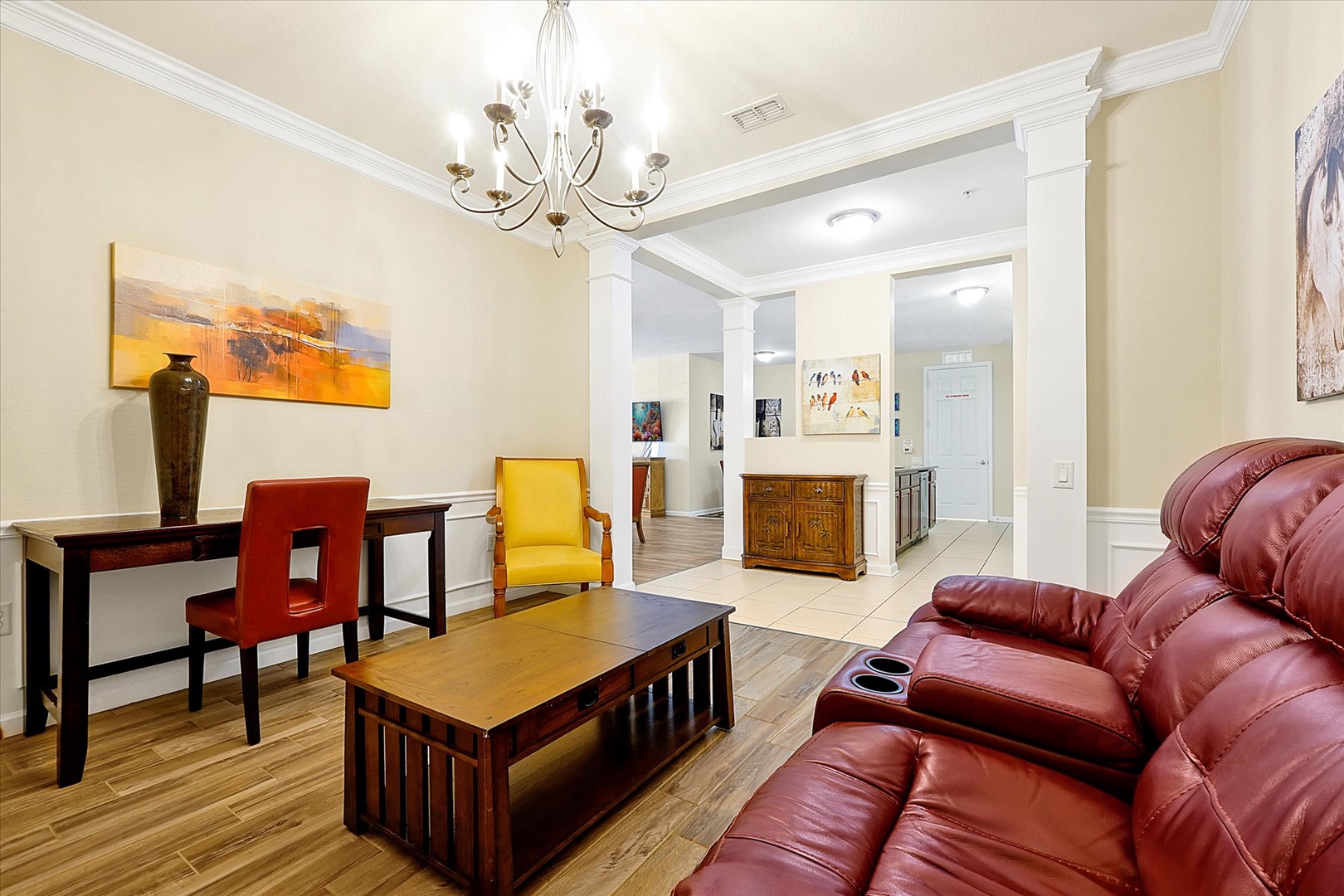 Relax in your spacious living area with rich leather seating, elegant chandelier, and vibrant art creating a warm, sophisticated atmosphere.