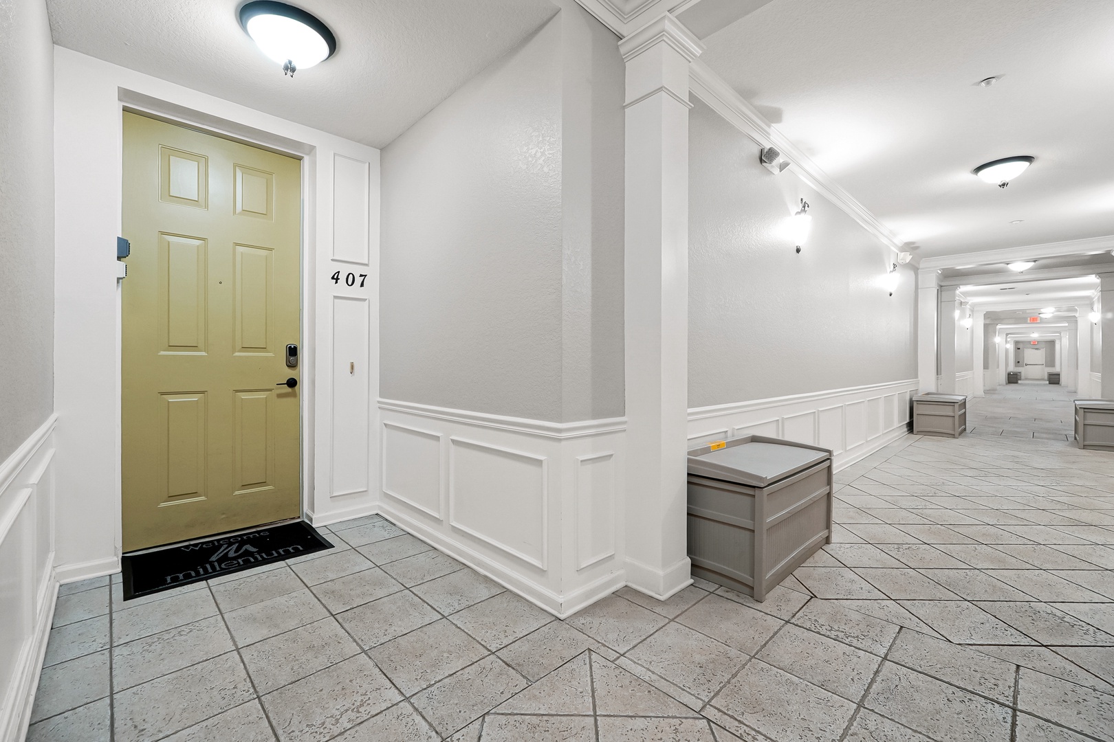 The property entrance features a bright, well-maintained hallway with elegant tile flooring and decorative wainscoting leading to unit 407. A clean, welcoming space marks your arrival.