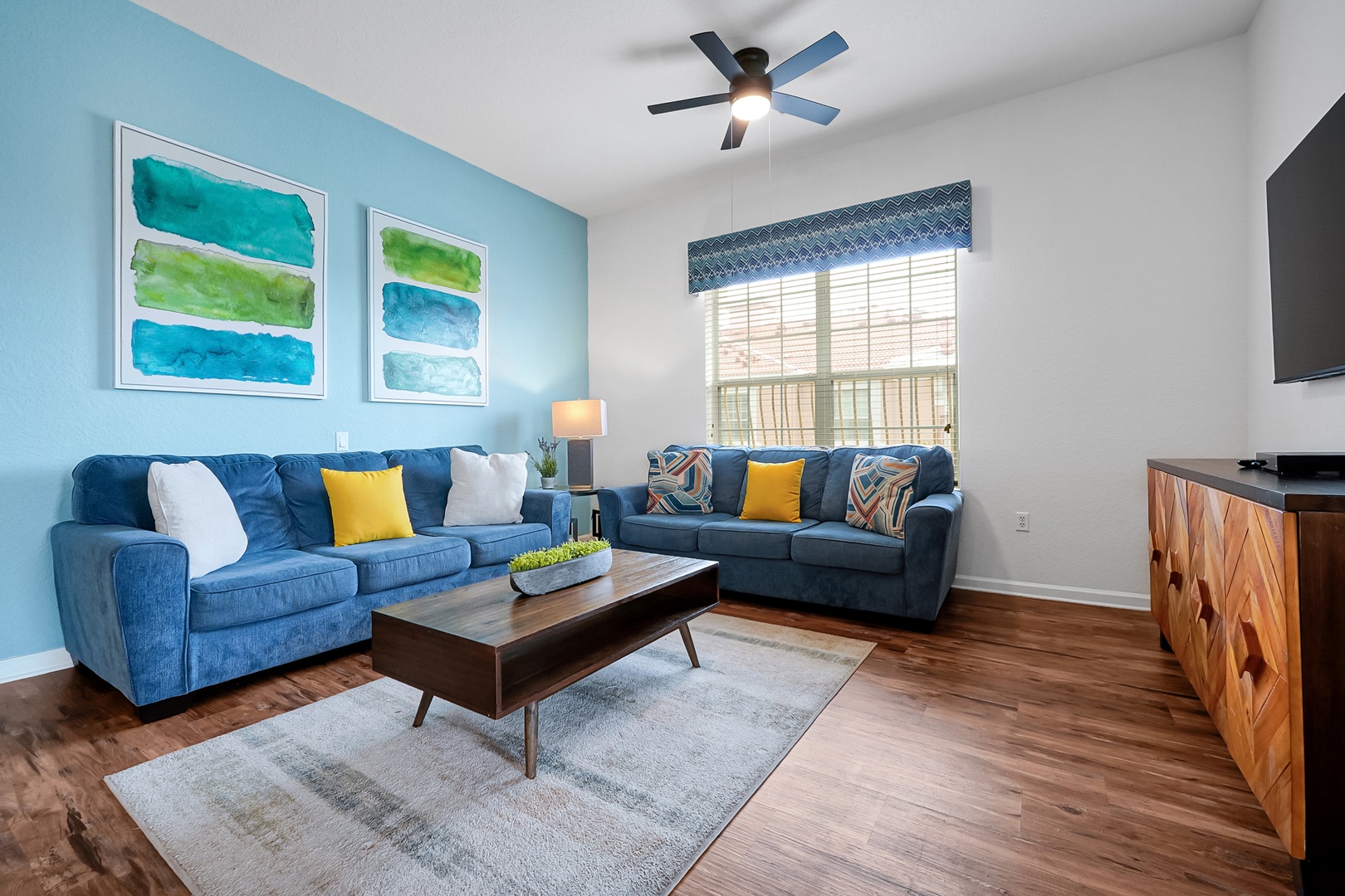 Settle into plush blue sofas with vibrant accent pillows and unwind in your bright, breezy living room—perfect for movie nights or lazy afternoons together.