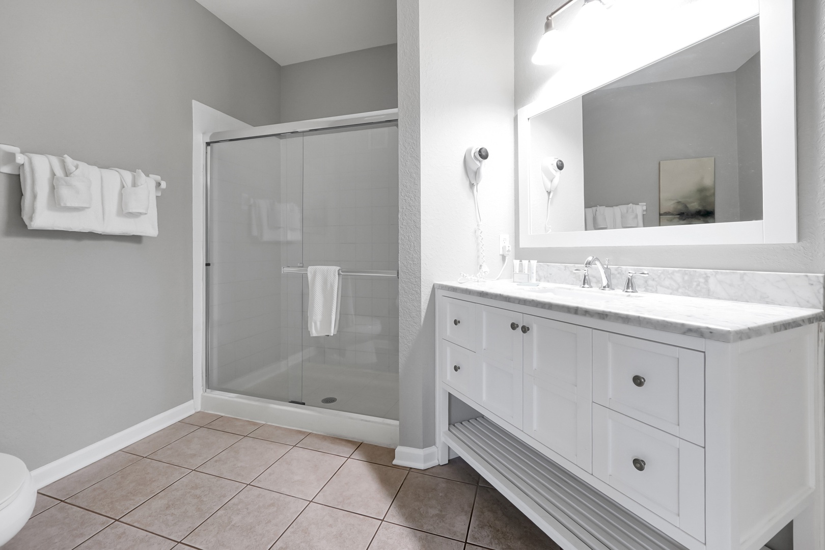 Step into your pristine bathroom where natural light fills the space, highlighting the marble countertop and walk-in shower—your private sanctuary after a day exploring the coast.