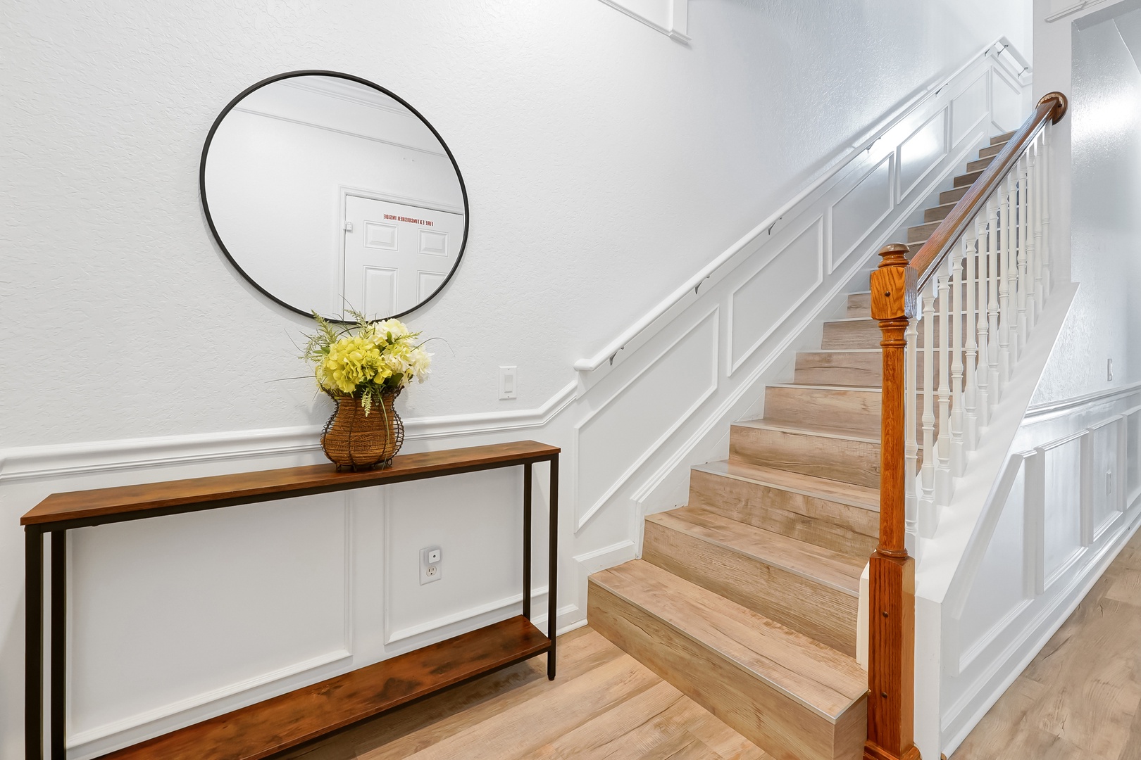 Your welcoming entryway features polished hardwood floors, elegant wainscoting, and a charming console table with fresh flowers to greet you home.