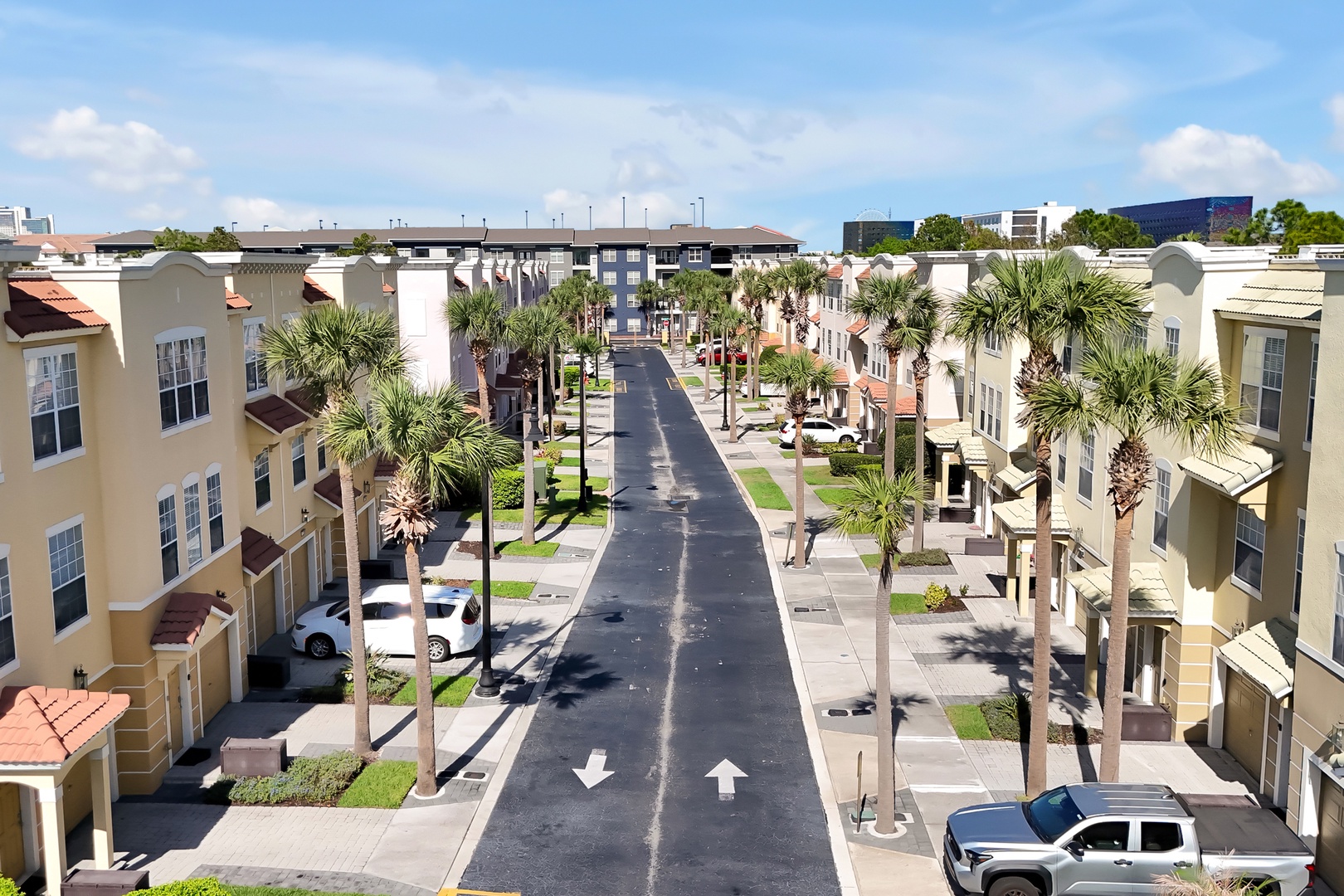 Aerial view of a well-planned residential community with palm-lined streets and modern townhomes in a tropical setting.