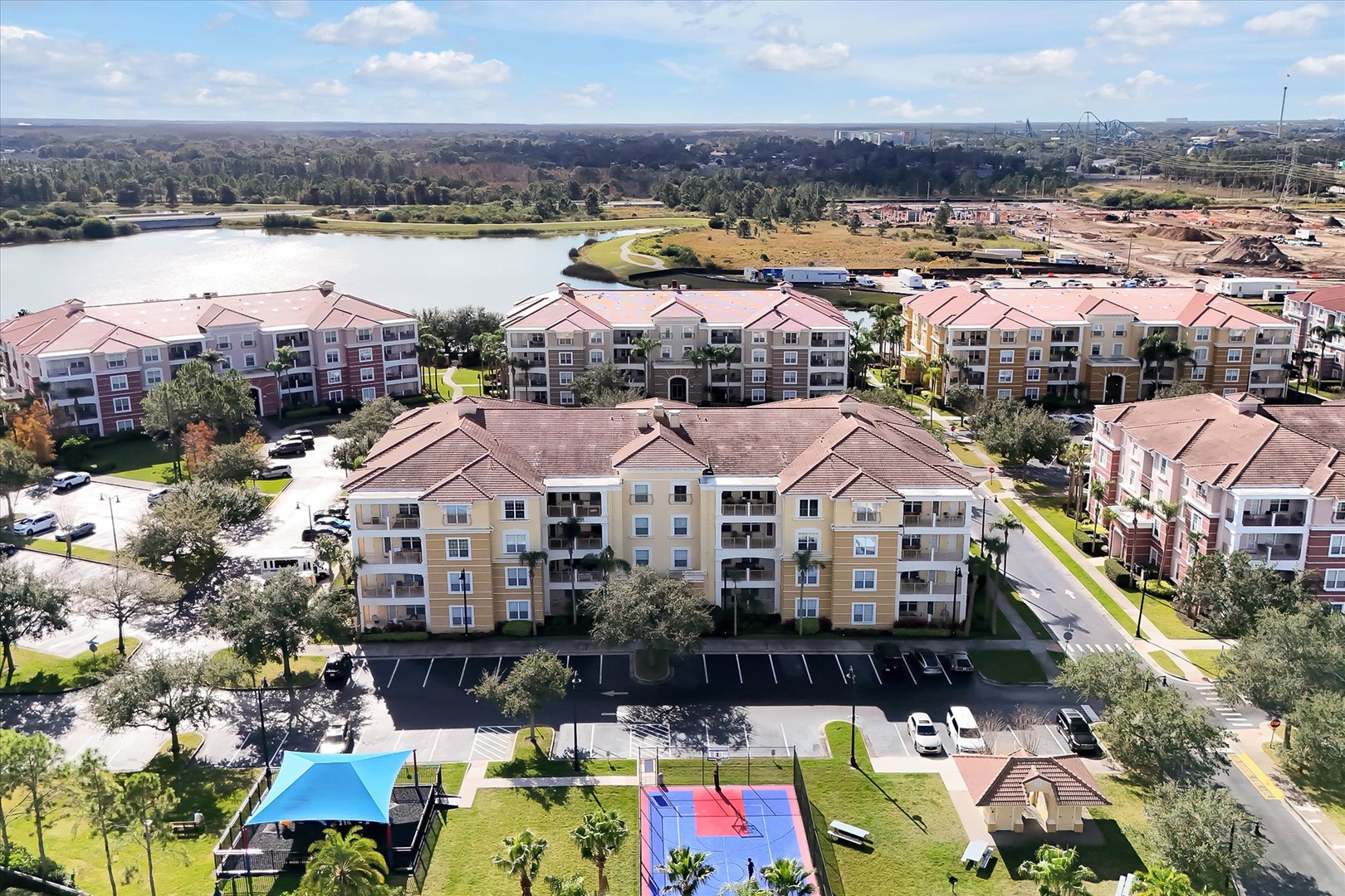 Aerial view of the resort community showcasing multi-story buildings with tile roofs, recreational courts, and nearby lake access.