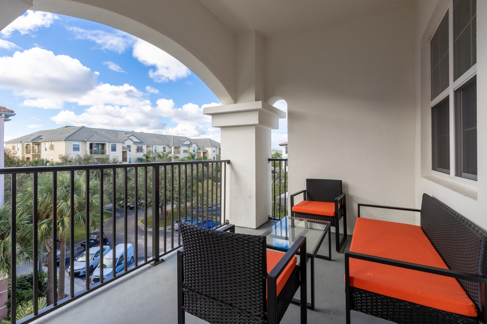 Step onto your private balcony where vibrant orange cushions invite relaxation while you overlook peaceful residential views.