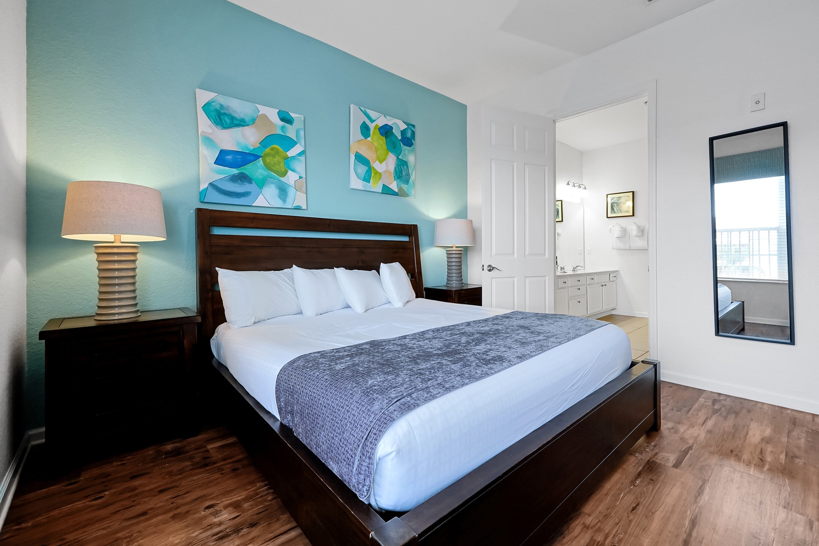 Step into your serene coastal retreat with its soothing turquoise accent wall and plush white bedding. Warm wood tones and soft lighting create an inviting atmosphere perfect for unwinding after your beach adventures.