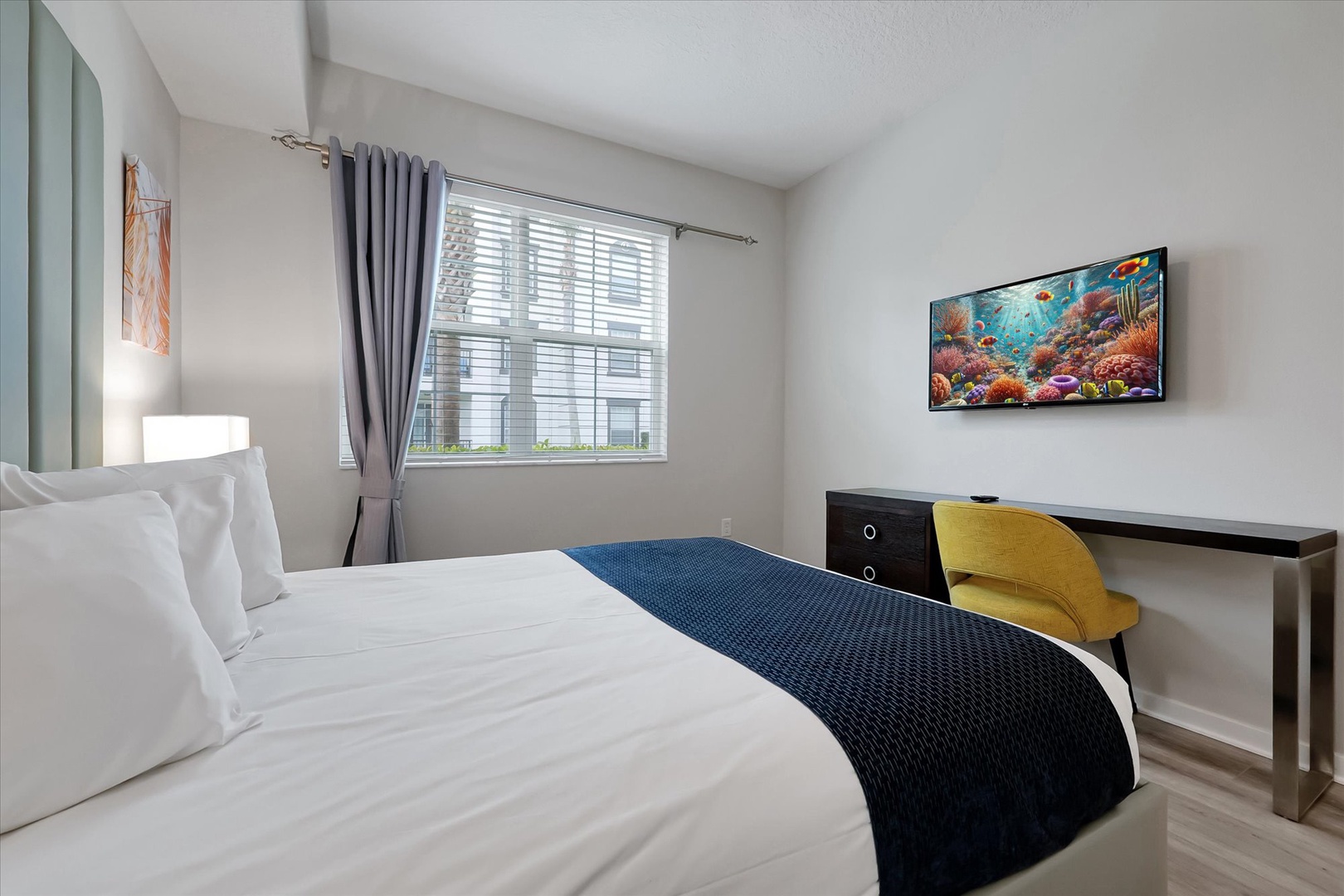 Rest peacefully in your bright, modern bedroom featuring crisp linens, a wall-mounted TV, and workspace desk for comfort.