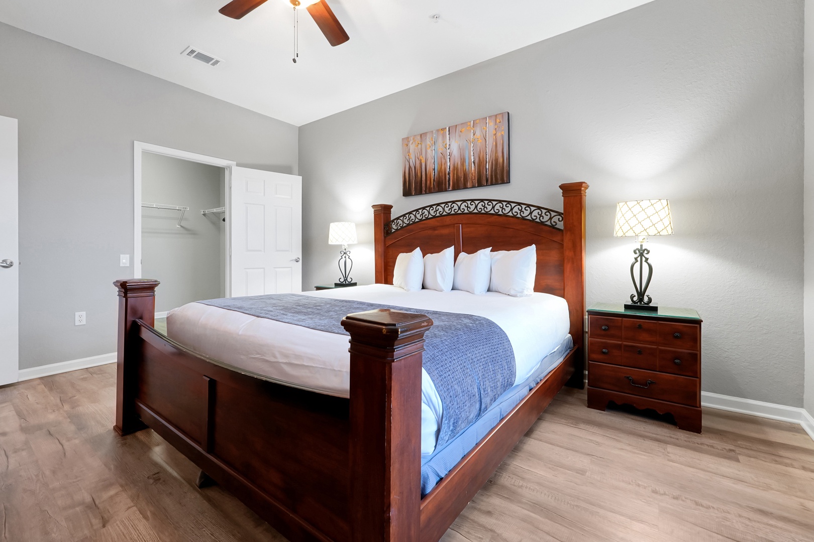 Sink into plush linens and drift off beneath the warm glow of bedside lamps, surrounded by elegant wood furnishings and peaceful gray tones that make this room your perfect retreat.