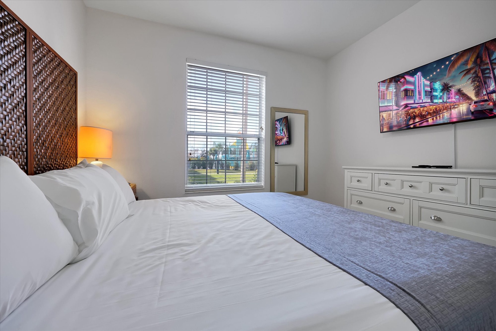 Unwind in your serene bedroom featuring crisp white linens, warm ambient lighting, and stylish tropical artwork that sets the perfect vacation mood.