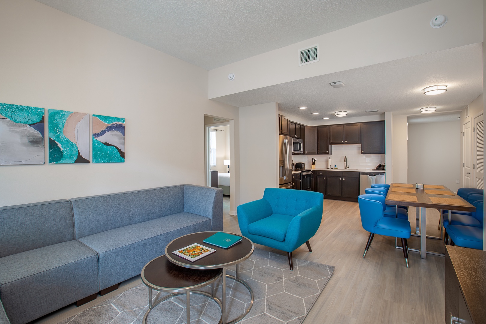 Relax in your stylish open-plan suite with modern kitchen, comfortable seating, and vibrant coastal artwork creating the perfect home-away-from-home atmosphere.