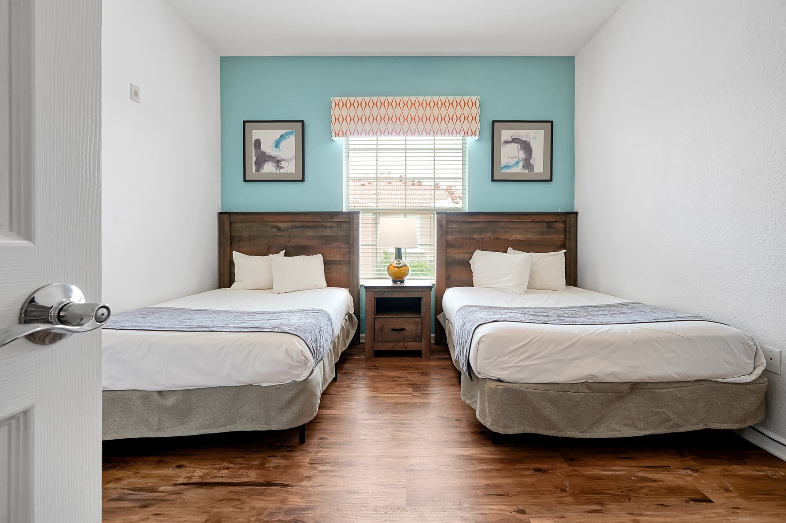 Unwind in this bright, cheerful bedroom with two plush beds and calming coastal decor. Natural light filters through the window, while the turquoise accent wall and warm wood floors create a welcoming retreat for your group.