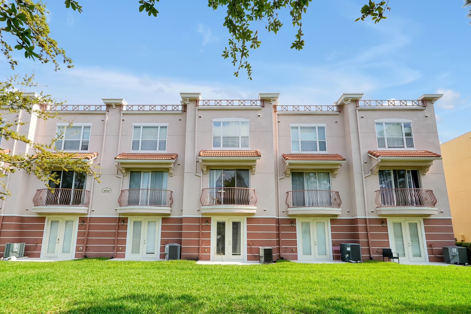 Modern townhouse-style property featuring private balconies, manicured lawn, and Mediterranean-inspired architecture.