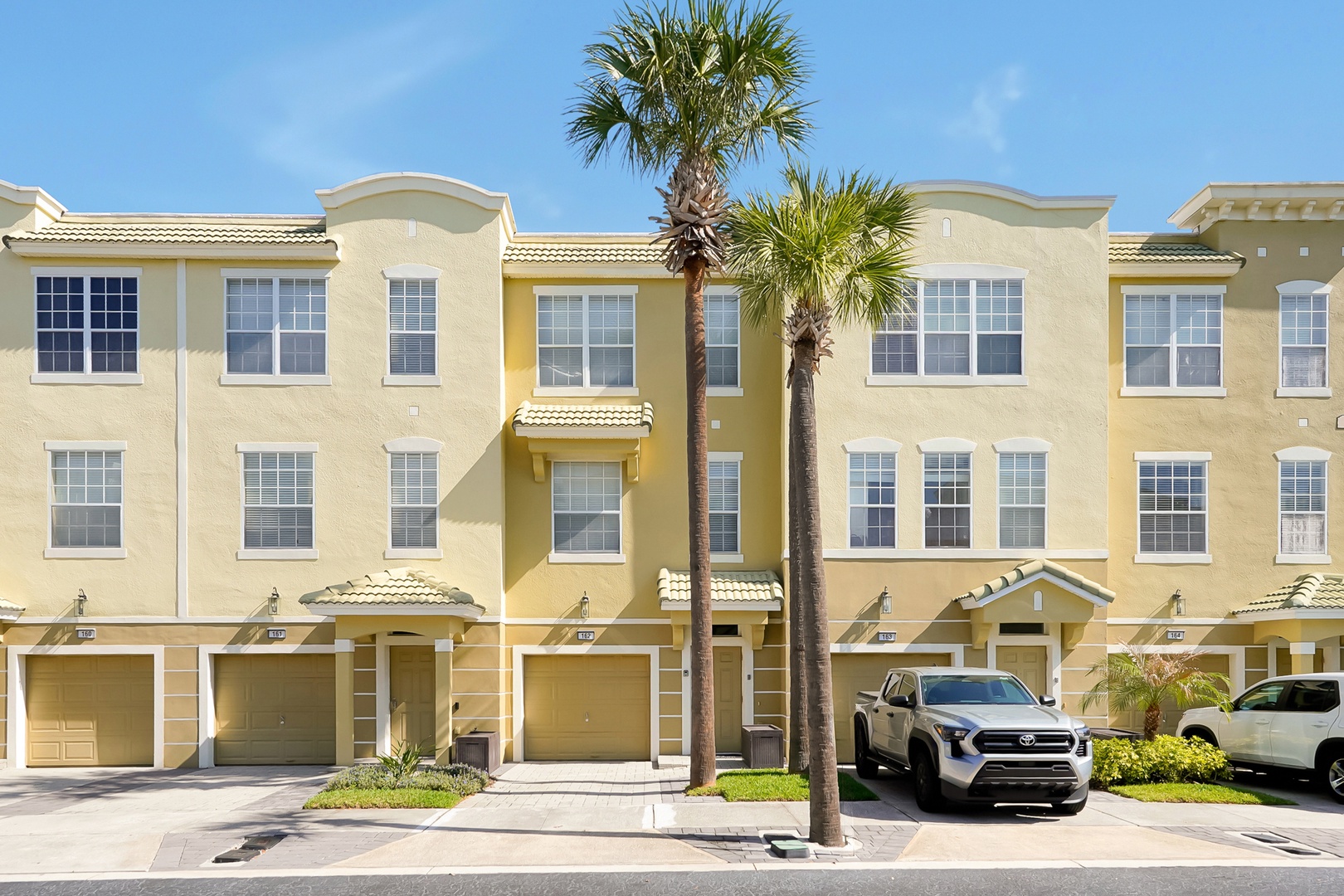 Modern Mediterranean-style townhomes with attached garages and tropical landscaping create a welcoming residential community.