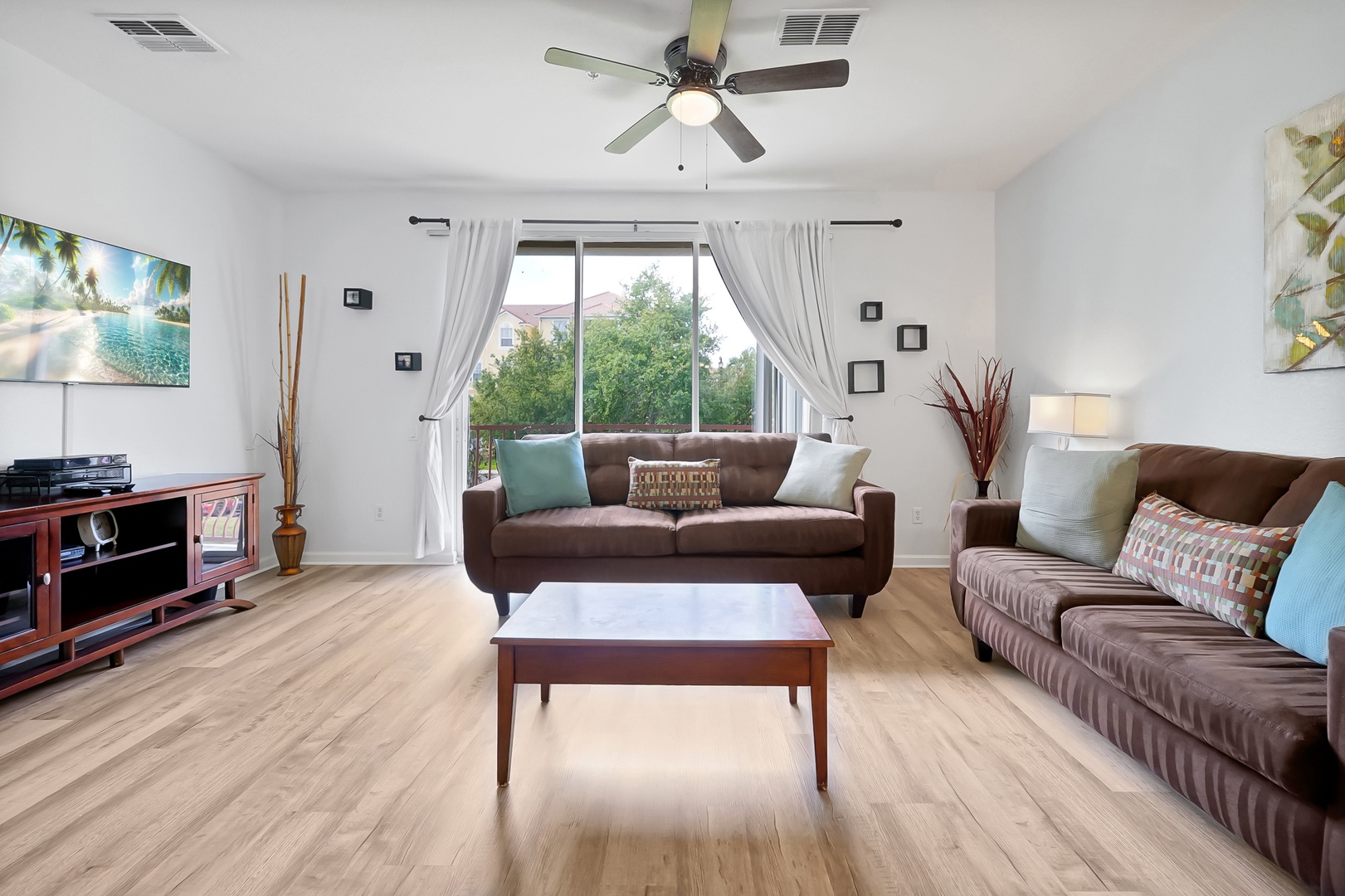 Relax in your bright, airy living space with comfortable seating, ceiling fan, and peaceful garden views through large windows.