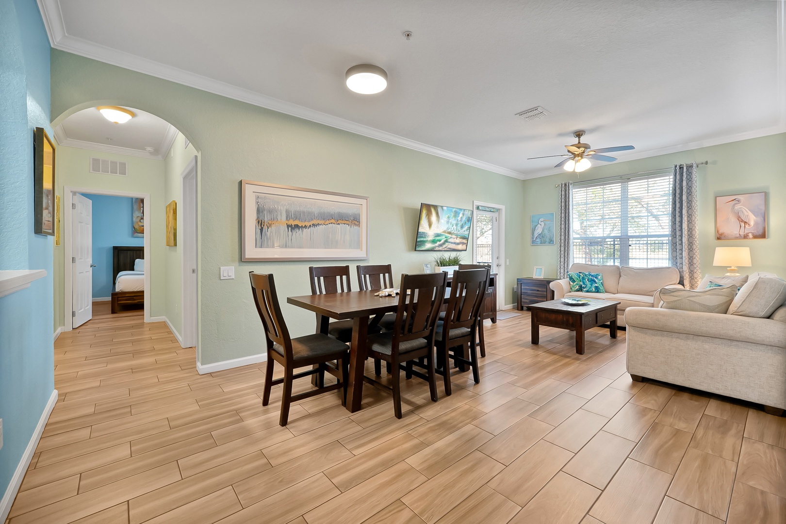 Your spacious open living area flows seamlessly from dining to relaxation, with warm wood floors and coastal artwork creating a welcoming atmosphere.