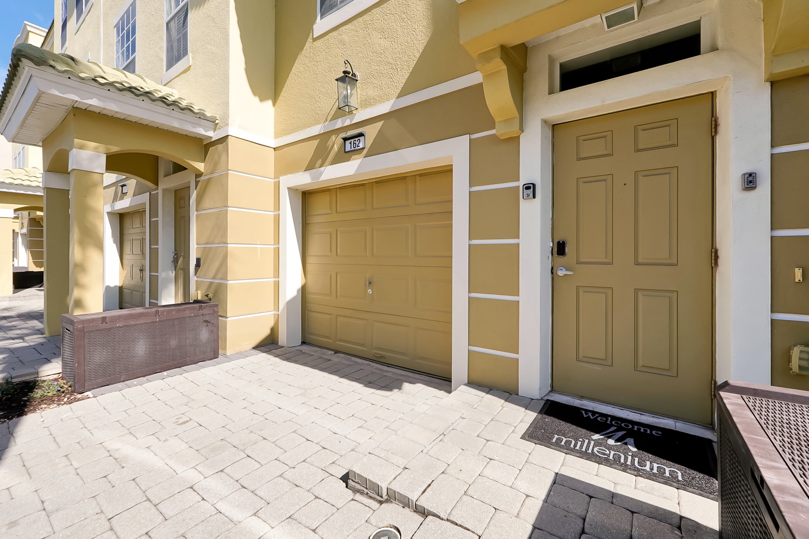 Bright Mediterranean-style townhome entrance with covered parking and elegant paver walkway welcoming guests to their vacation retreat.