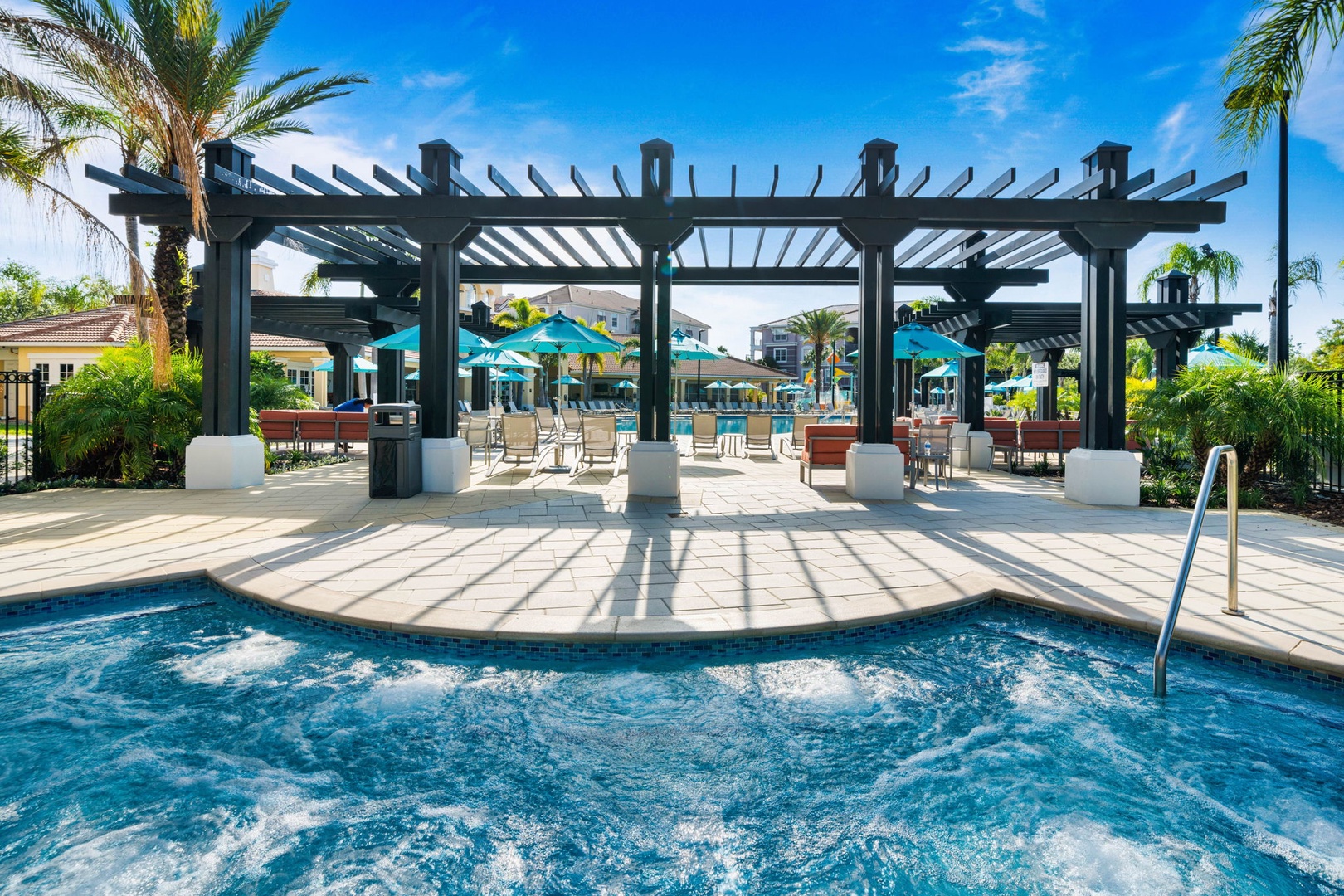 The poolside pergola and bubbling spa create a resort-like oasis surrounded by palm trees and turquoise umbrellas, perfect for sunny days and warm evenings under the open sky.