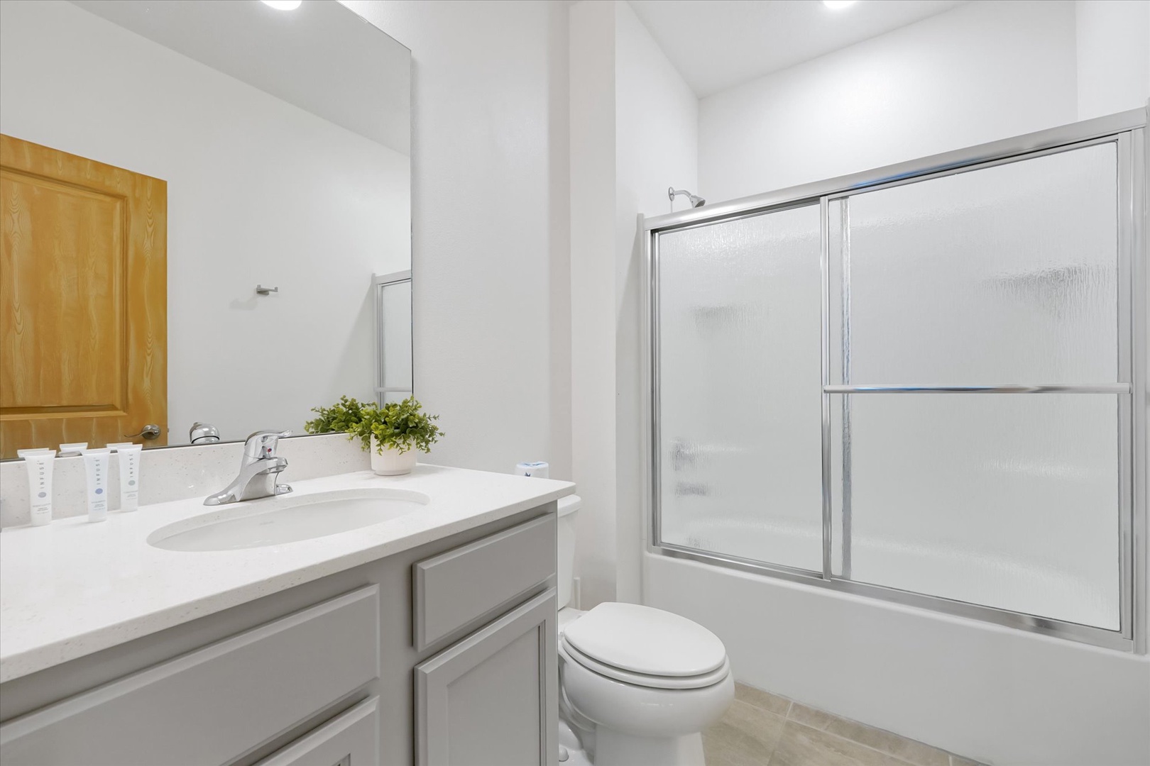 Step into your bright, pristine bathroom featuring a spacious vanity, tub-shower combo with frosted glass doors, and all the essentials for your comfort—fresh towels, toiletries, and thoughtful details await.