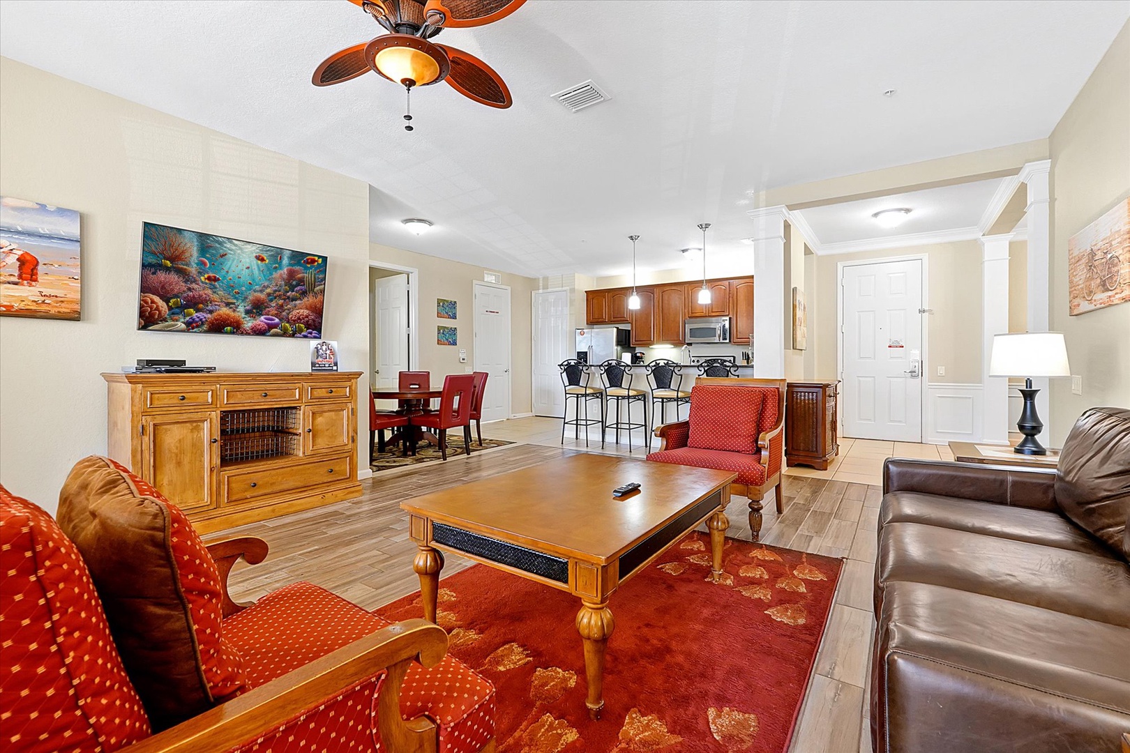 Relax in your open-concept living space featuring warm wood furnishings, leather seating, and vibrant coral artwork that creates a coastal ambiance.