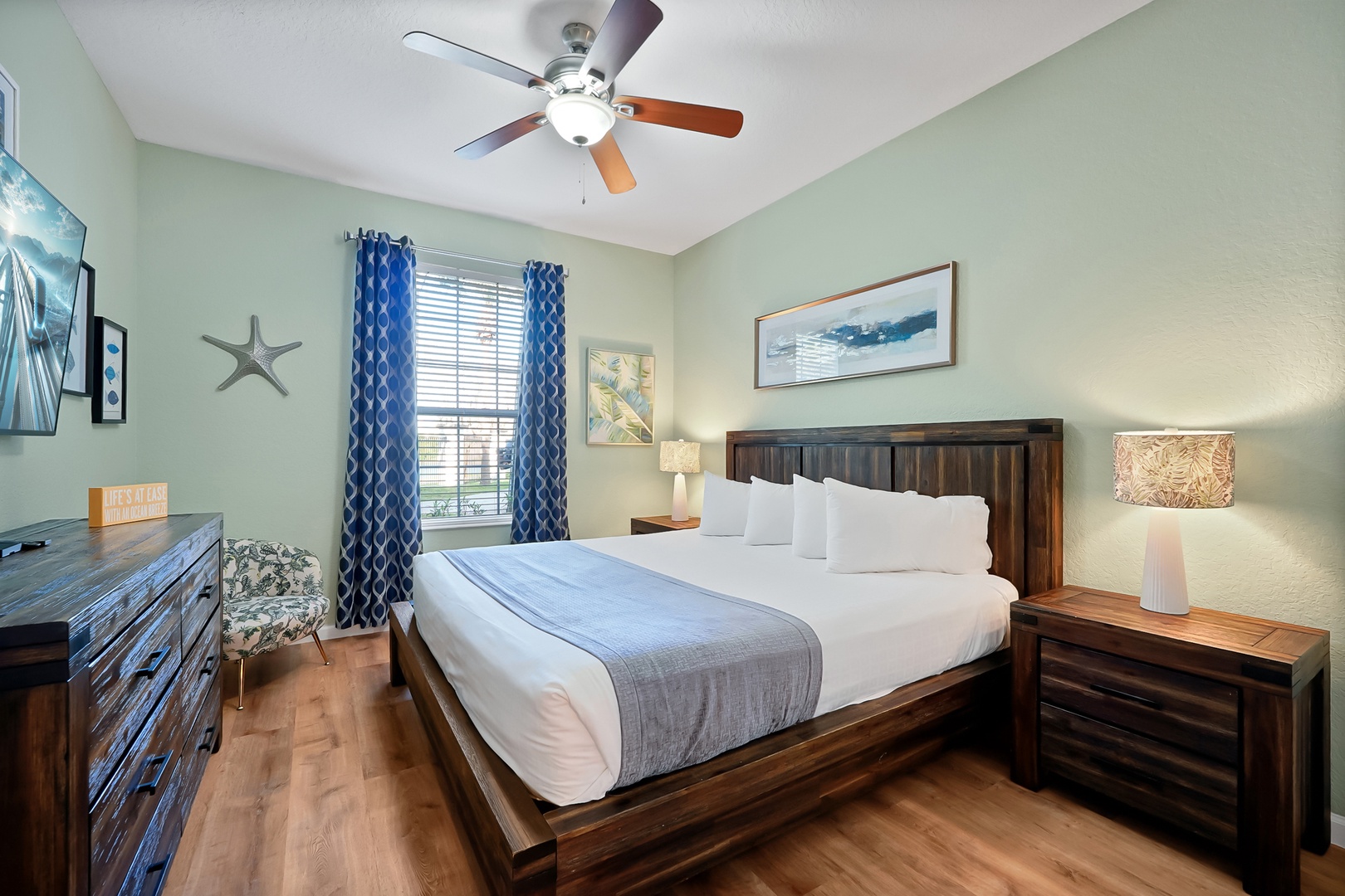 Drift off in your tranquil coastal-themed bedroom featuring a plush king bed, gentle ceiling fan, and warm wood furnishings.