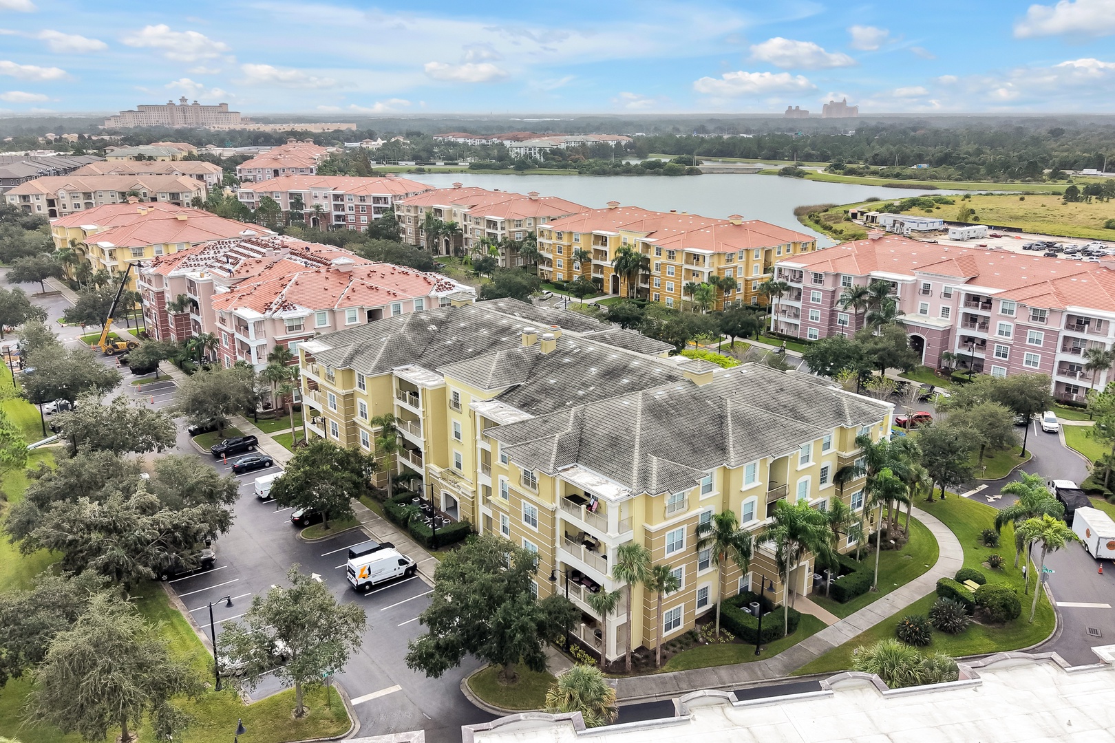 An aerial view of the property showcasing colorful multi-story buildings amid lush landscaping, with a peaceful lake and surrounding resort community visible in the background.