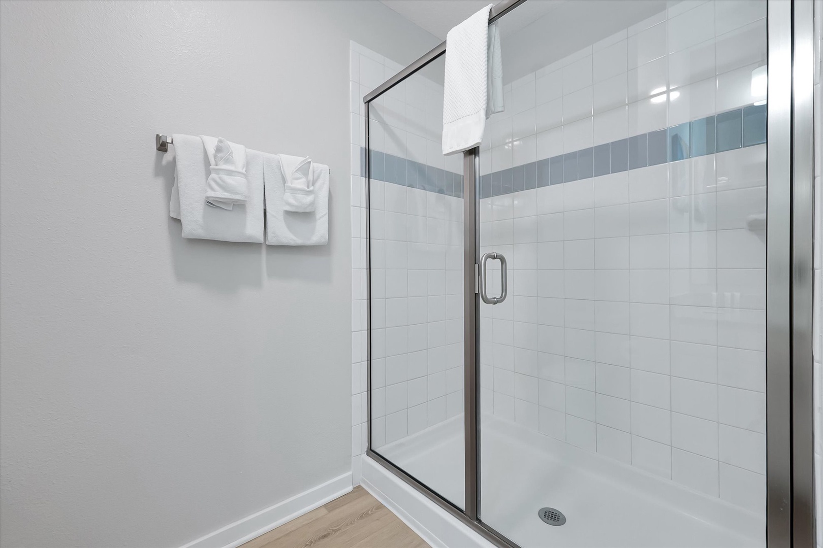 Step into your pristine glass-enclosed shower with elegant white tiles and soothing blue accents, where fresh towels await your refreshing start.