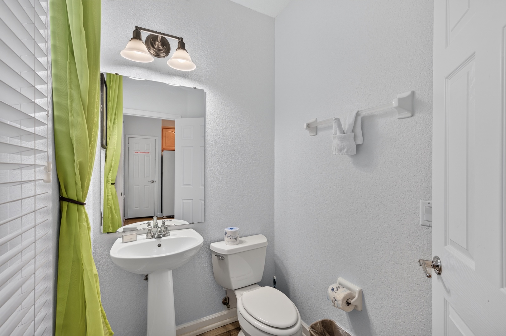 Step into your bright, clean bathroom with a pedestal sink and fresh towels waiting. The cheerful green curtain adds a welcoming pop of color to your private space.