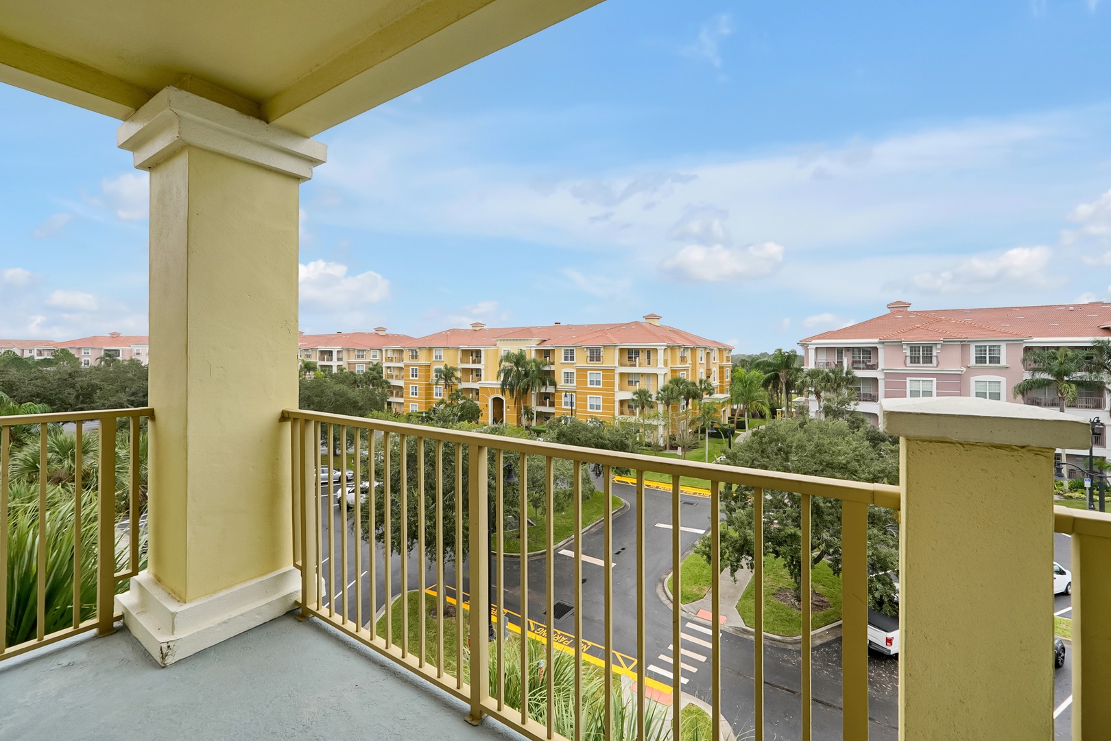 The covered balcony offers a peaceful overlook of the tropical community, with palm trees and colorful buildings creating a serene Florida atmosphere.