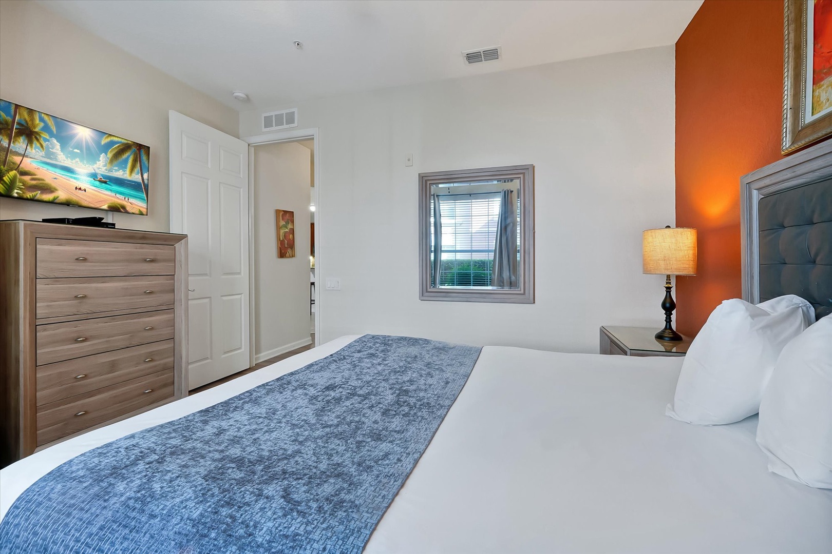 Your comfortable bedroom features a warm orange accent wall, plush bedding, and tropical artwork to help you unwind after your adventures.