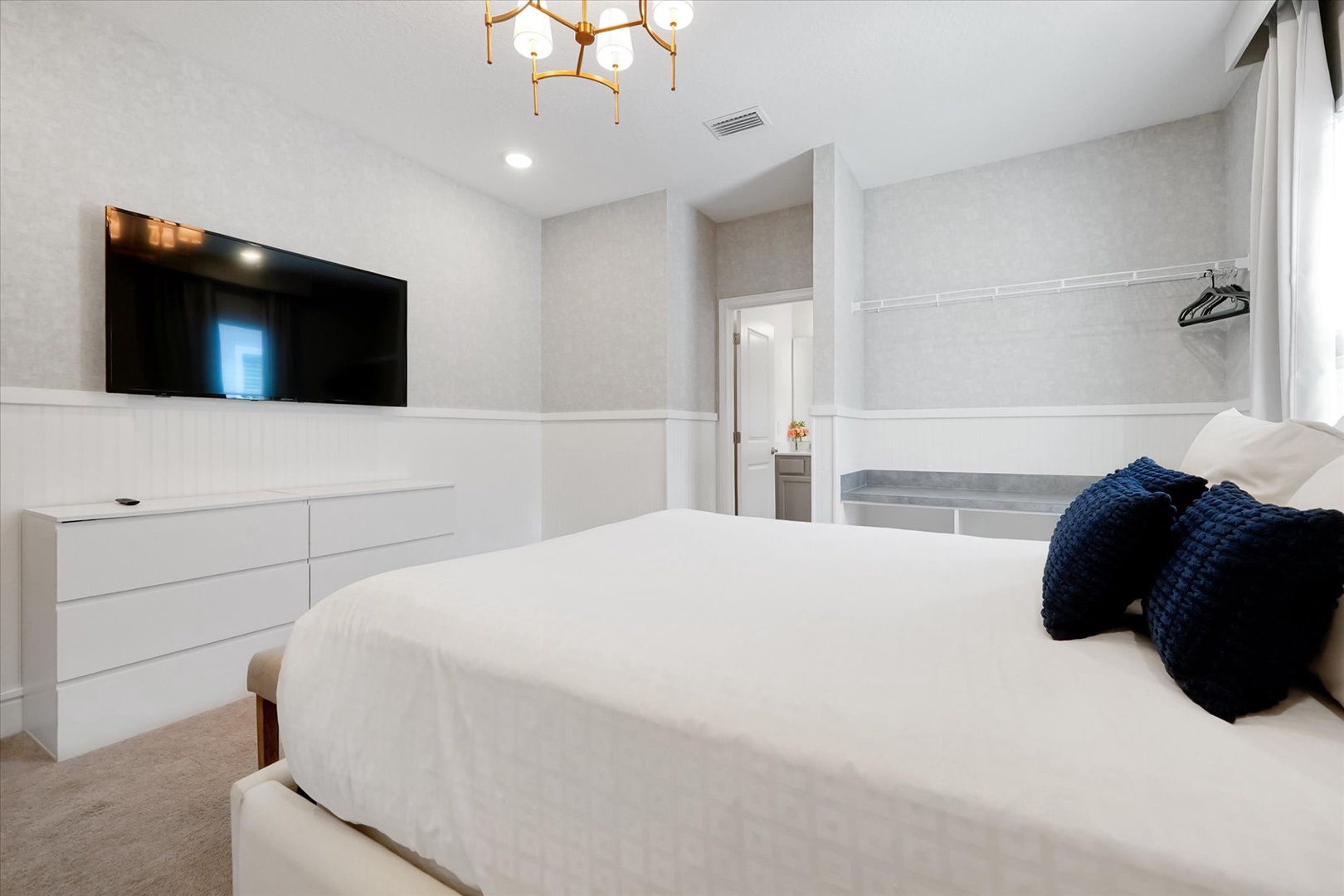 Sink into crisp linens and unwind beneath a modern gold chandelier. Your wall-mounted TV invites cozy movie nights after a day of exploring.