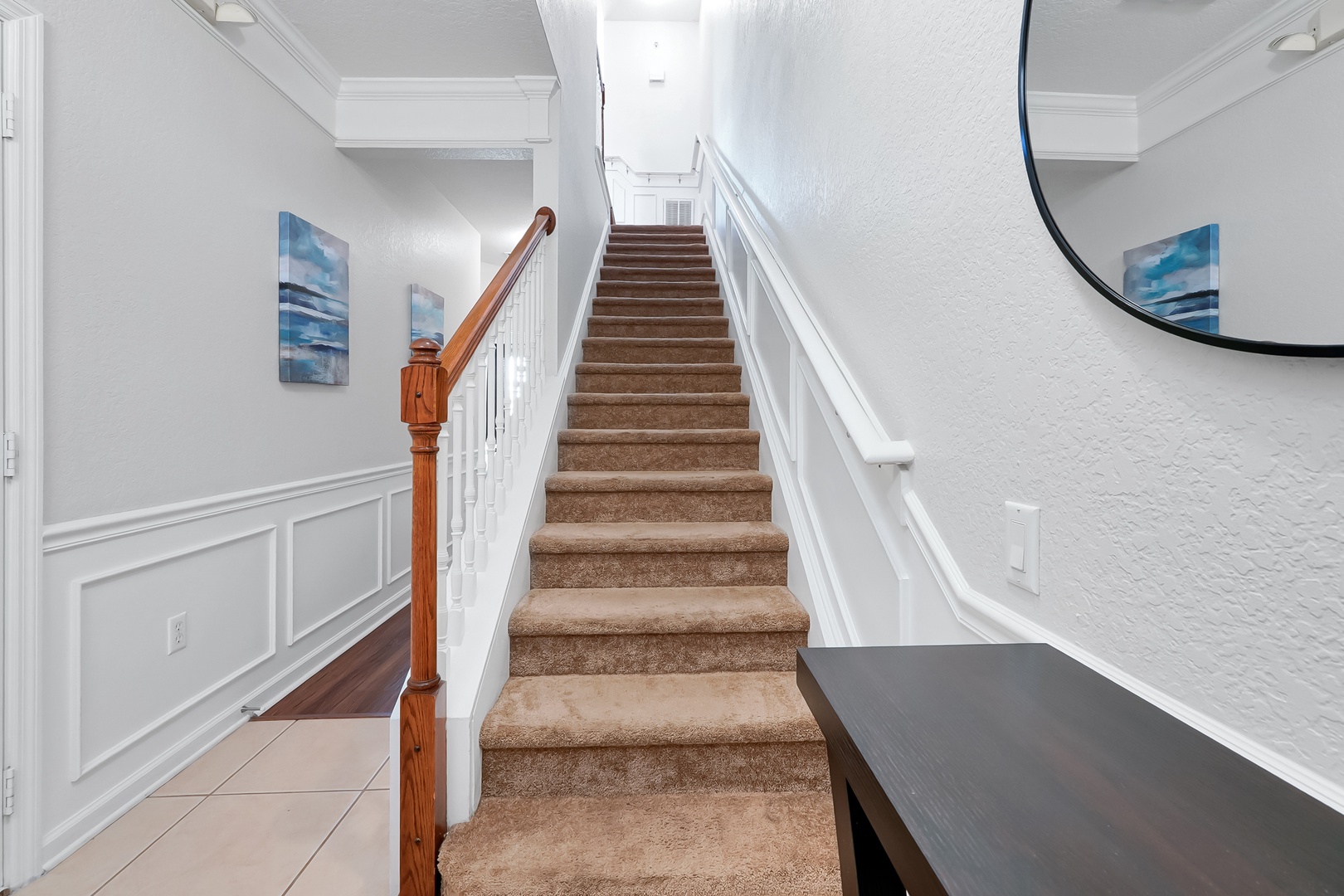 Ascend carpeted stairs to your upper-level retreat, surrounded by elegant wainscoting and calming coastal artwork.