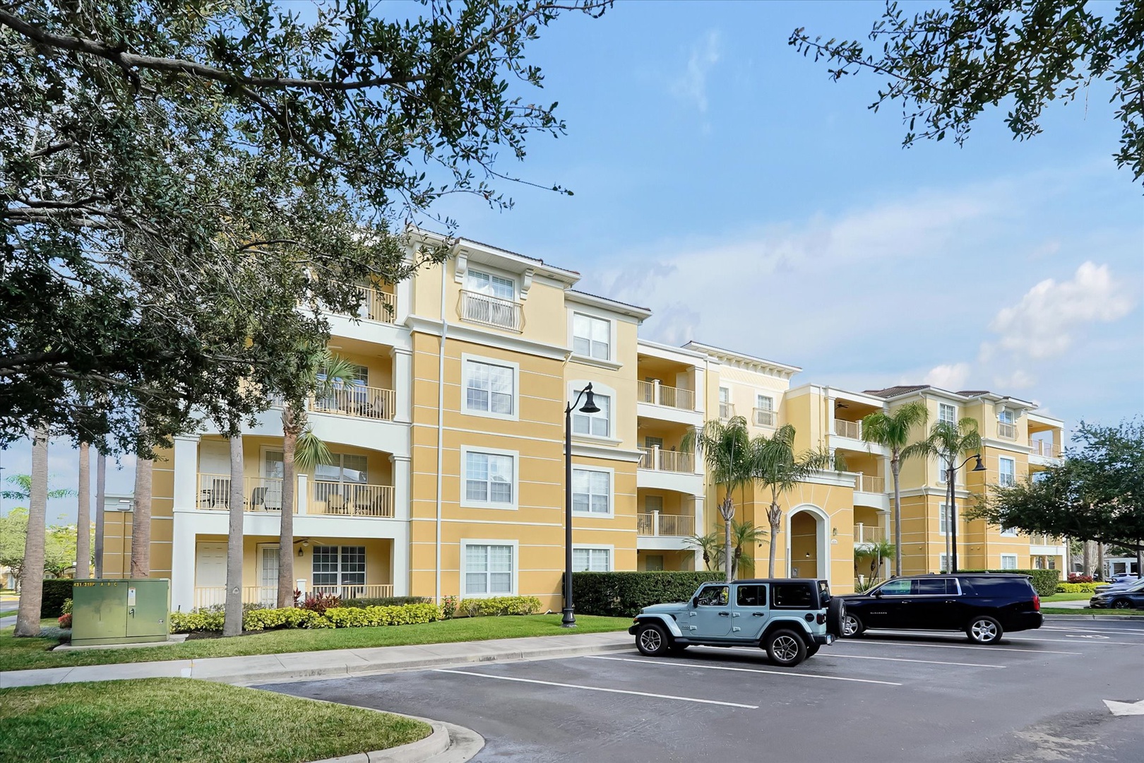 This charming yellow resort building offers comfortable accommodations with private balconies surrounded by lush tropical landscaping and palm trees.