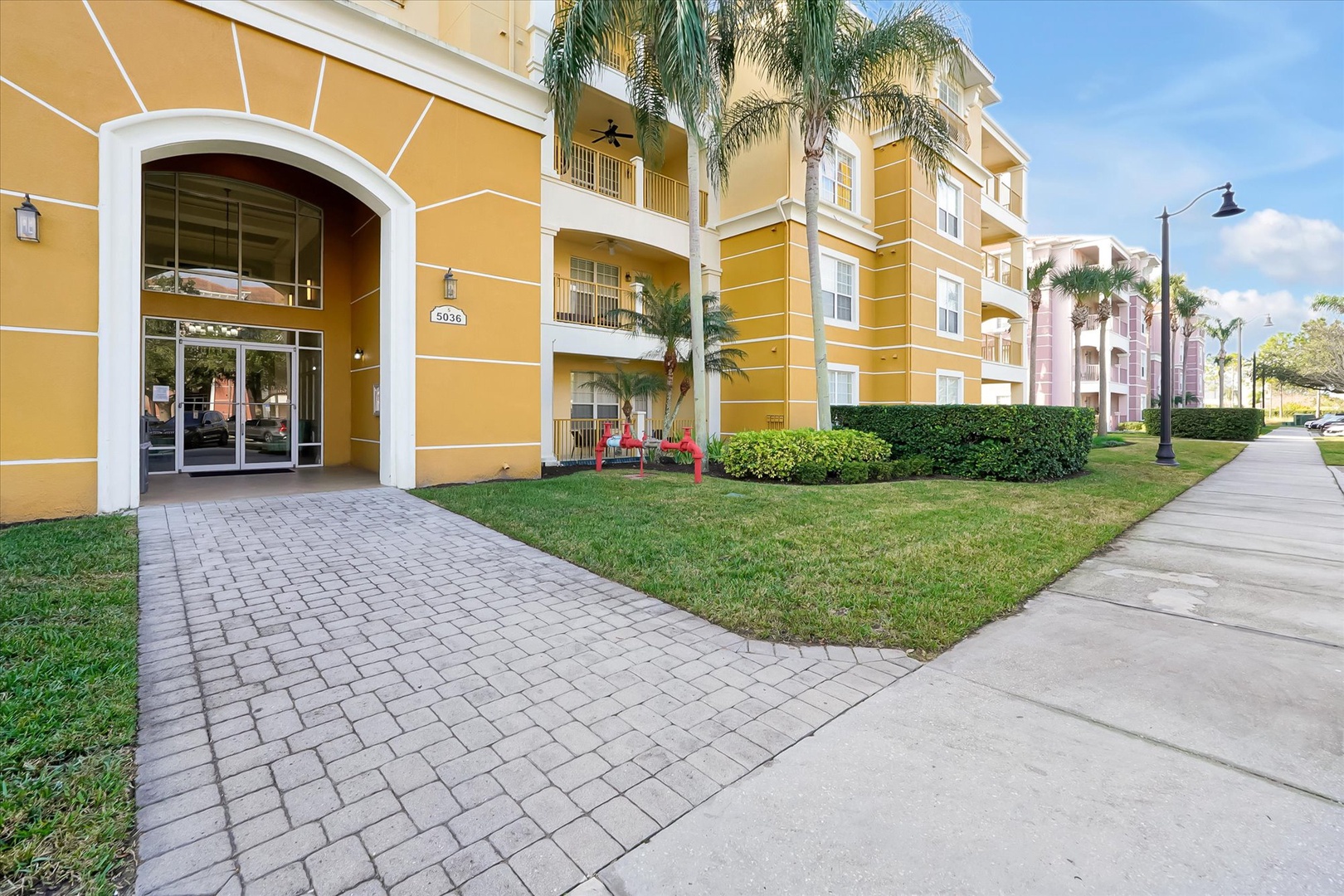 Sunny resort entrance with tropical palm trees and manicured landscaping welcomes guests to this vibrant vacation community.