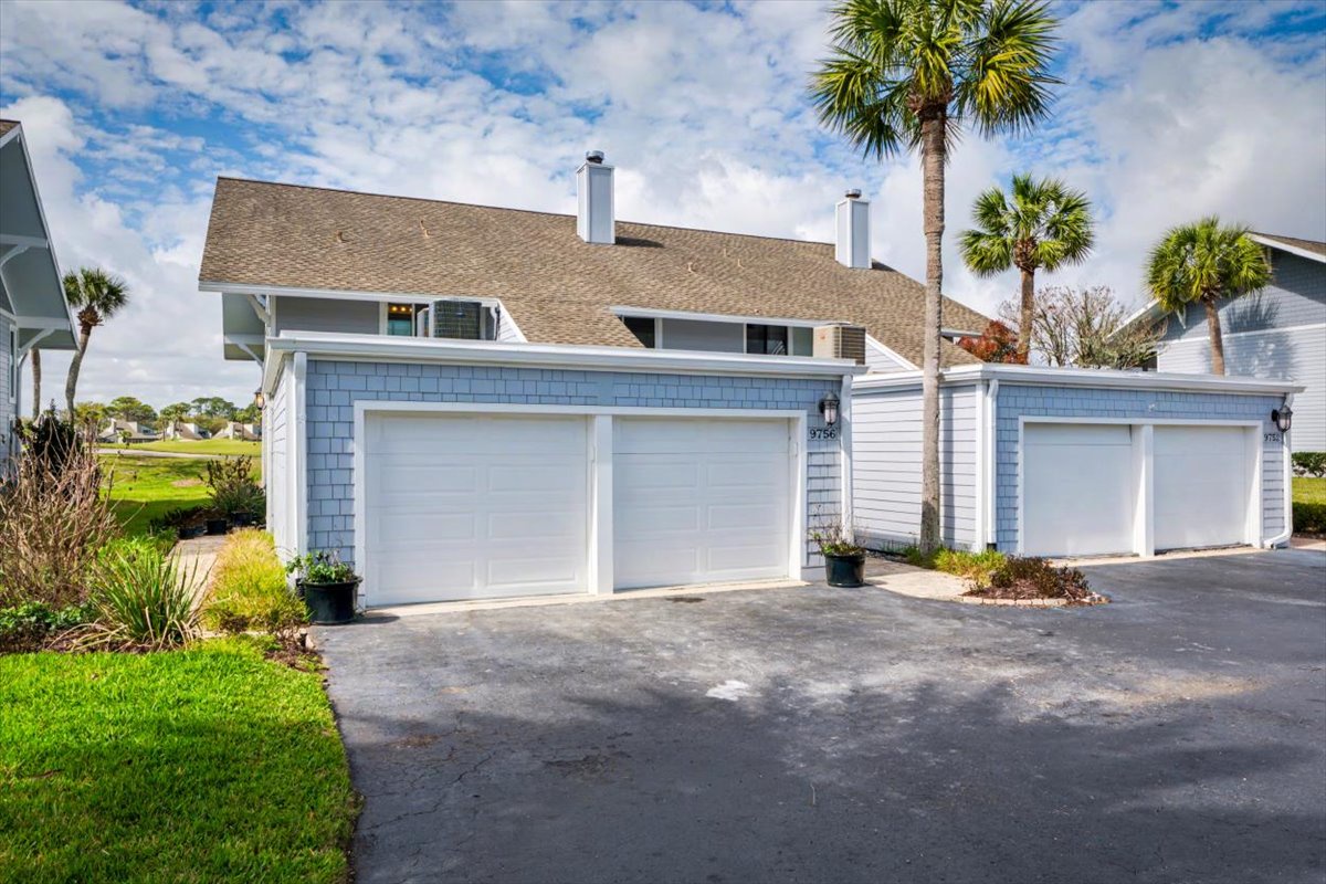 Coastal-style townhome with attached two-car garage and tropical landscaping in a well-maintained residential community.