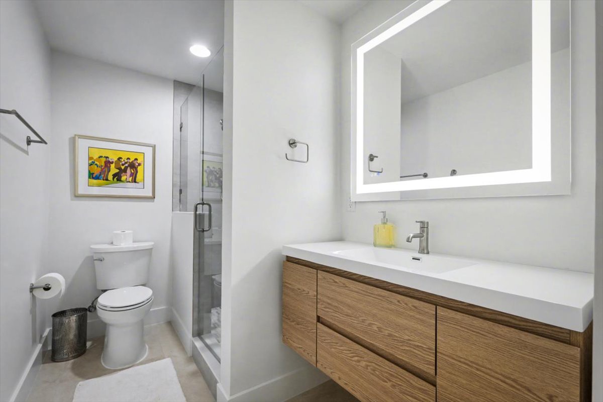 Your sleek bathroom features a spacious vanity with warm wood cabinetry, illuminated mirror, and glass-enclosed shower for refreshing starts.