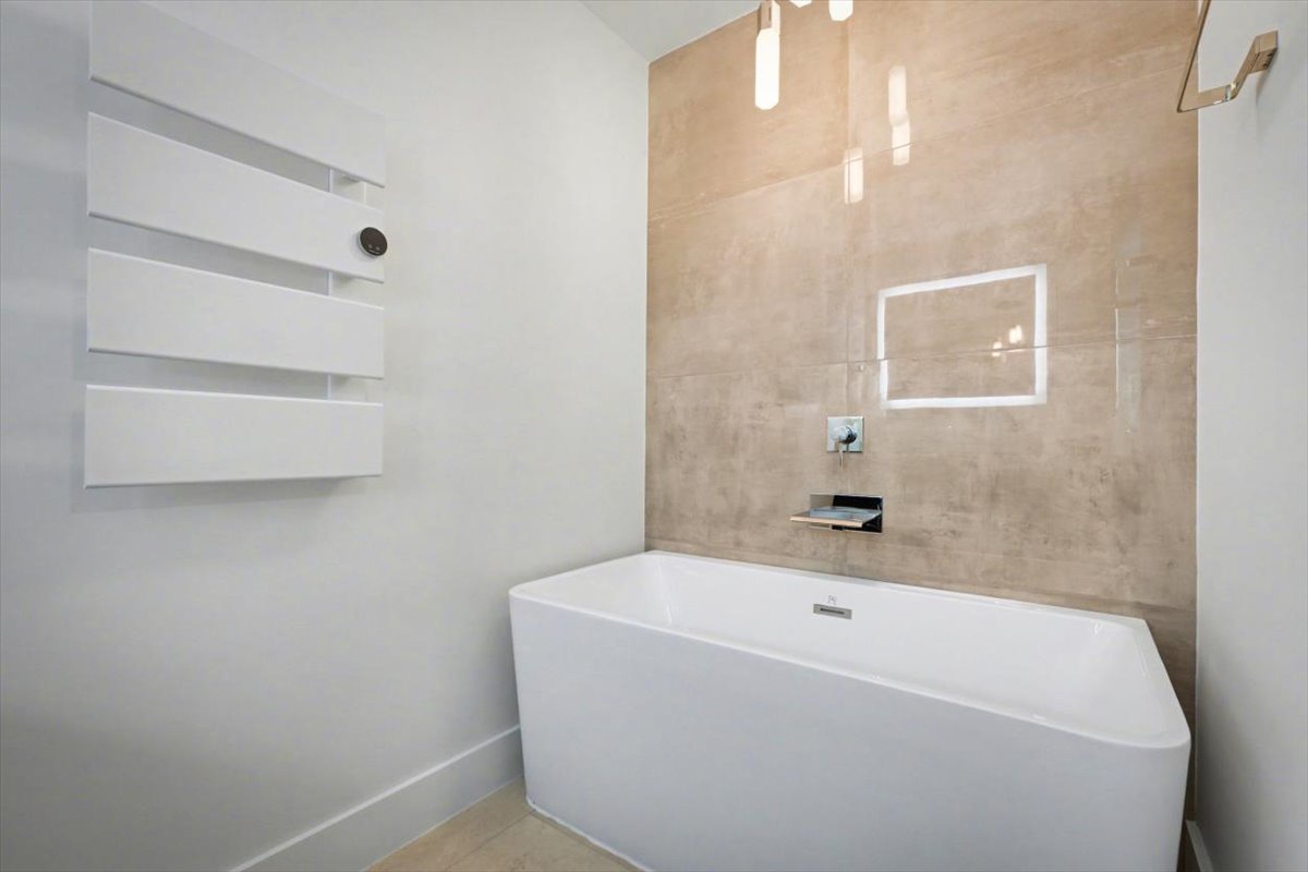 Sink into this luxurious soaking tub, where warm stone tiles and modern elegance create your perfect retreat for unwinding.