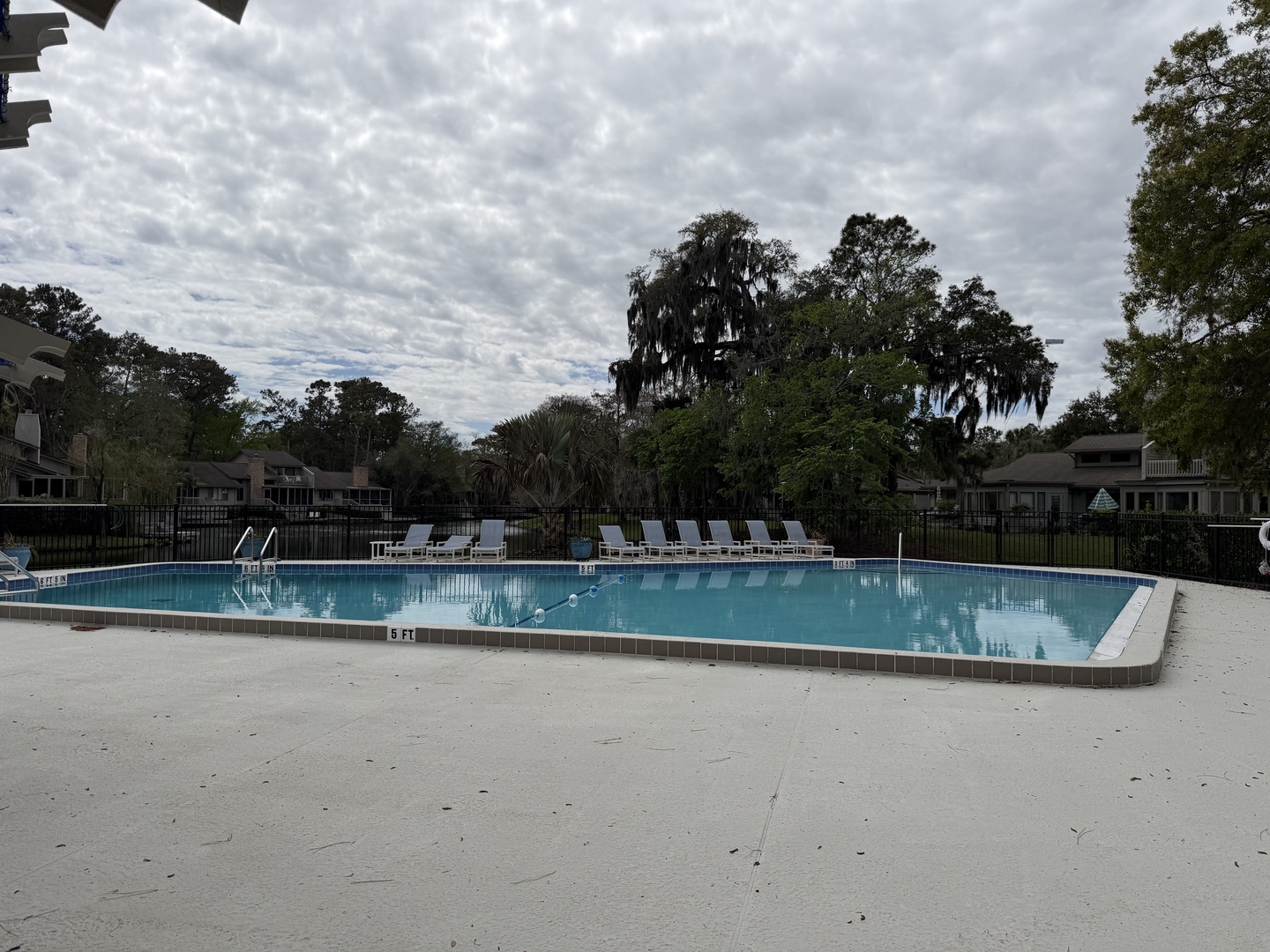 Community pool surrounded by lush trees and residential buildings under a dramatic cloudy sky.