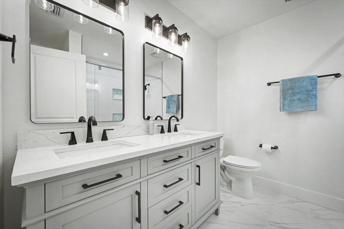 Your elegant bathroom features a double vanity with marble countertops, stylish black fixtures, and crisp white finishes for a spa-like retreat.