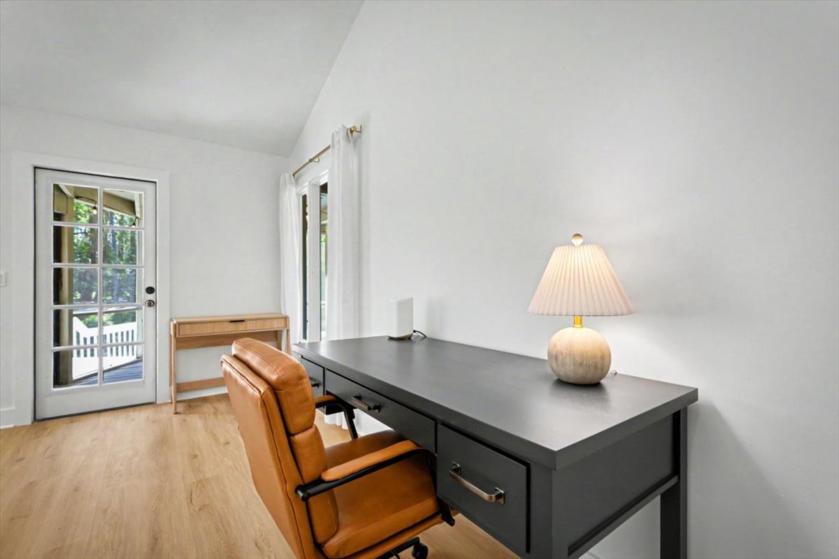 Your bright office space features a stylish desk with warm lamp lighting, leather seating, and French doors opening to outdoor views.