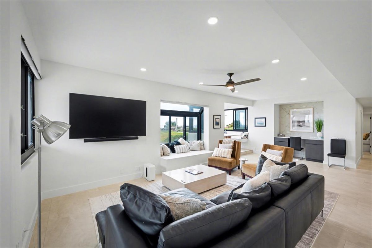 Unwind in your spacious living room featuring modern furnishings, a large TV, and abundant natural light from expansive windows.