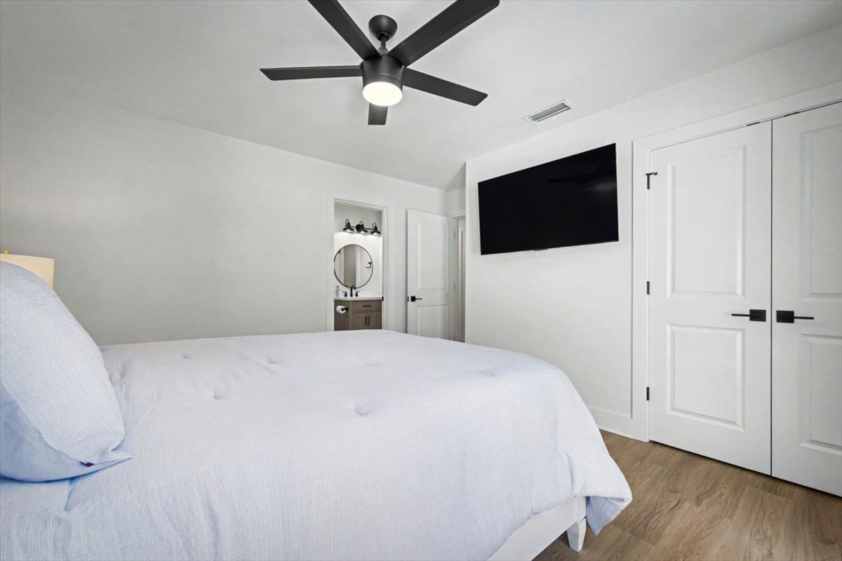 Unwind in your serene bedroom sanctuary with plush bedding, modern ceiling fan, and wall-mounted TV for your comfort and entertainment.