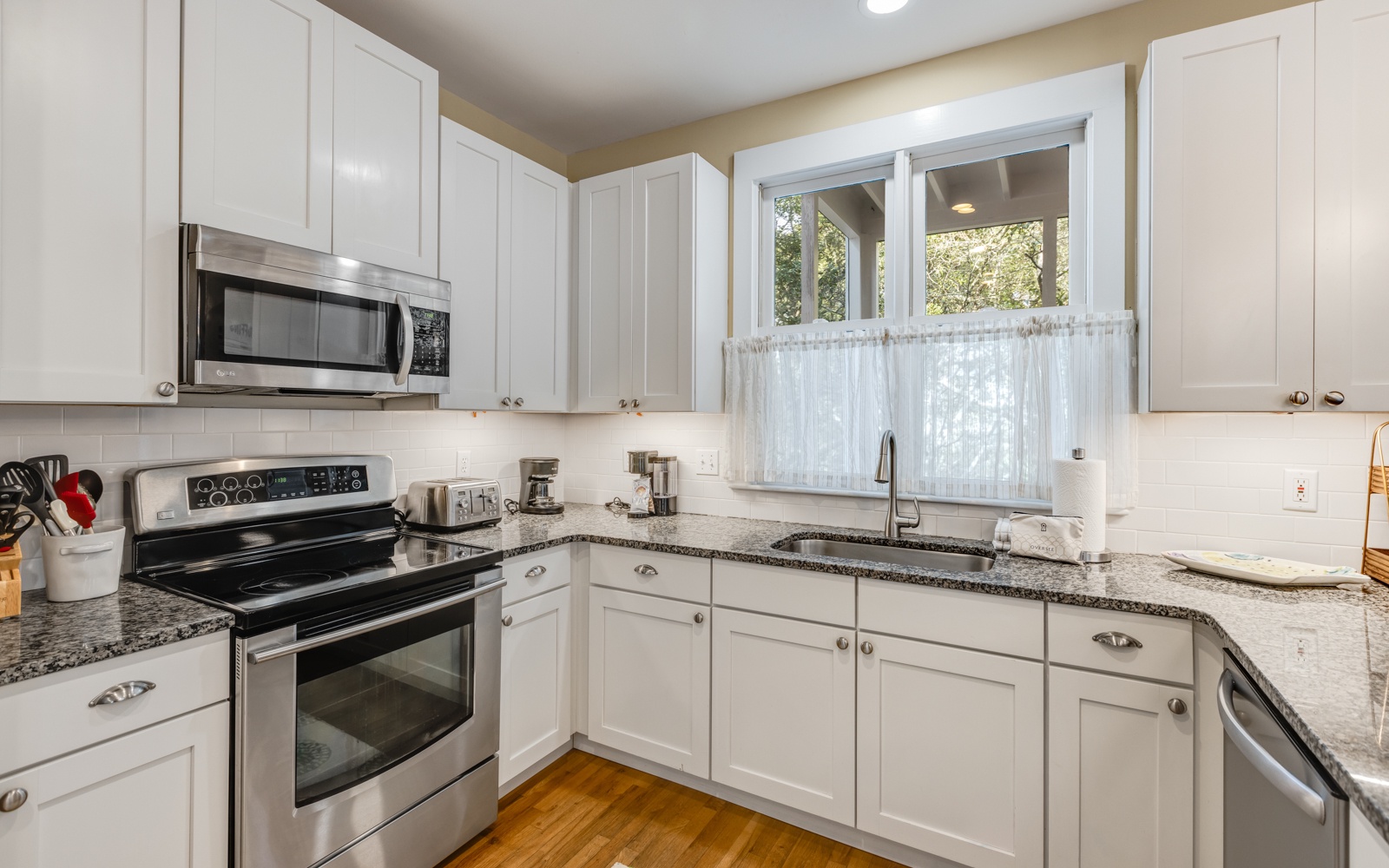 Your fully equipped kitchen awaits with granite counters, stainless appliances, and charming garden views through the window.