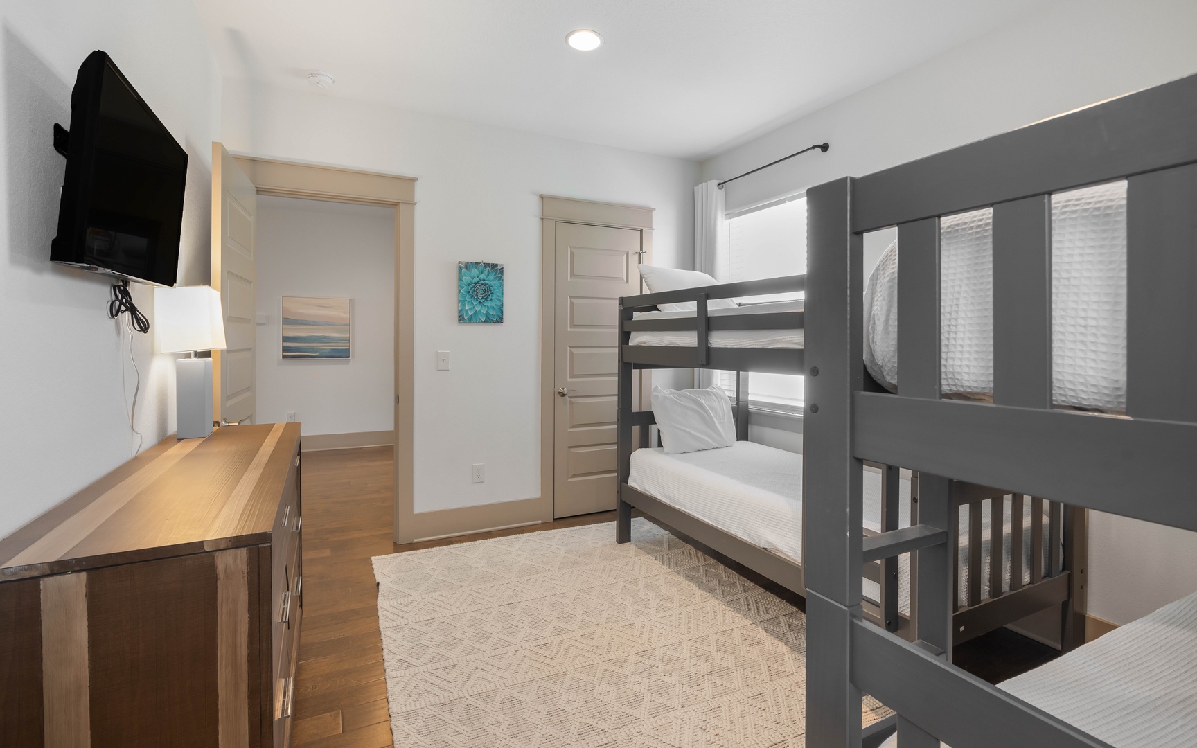 Your cozy bunk room features crisp white linens, warm wood accents, and a wall-mounted TV for evening entertainment in this thoughtfully designed space.