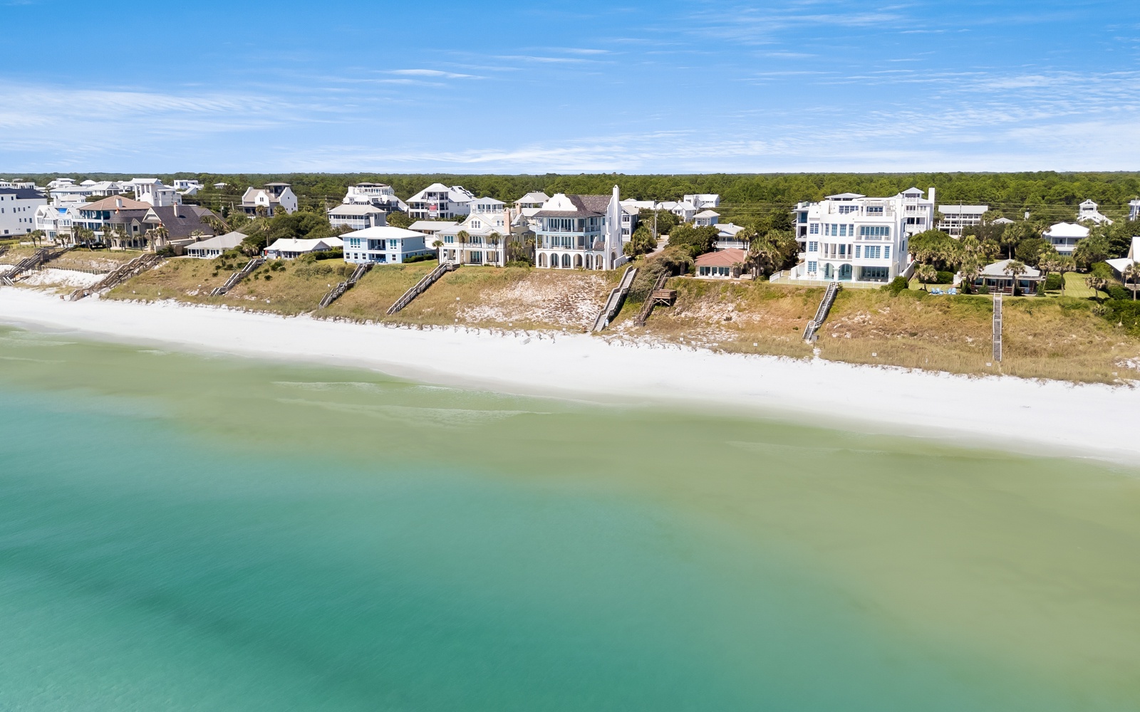 Stunning beachfront properties line pristine white sand shores with crystal-clear turquoise waters stretching to the horizon.