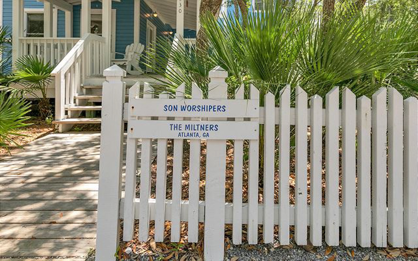 Charming coastal property entrance with personalized gate sign and tropical landscaping in a peaceful residential setting.